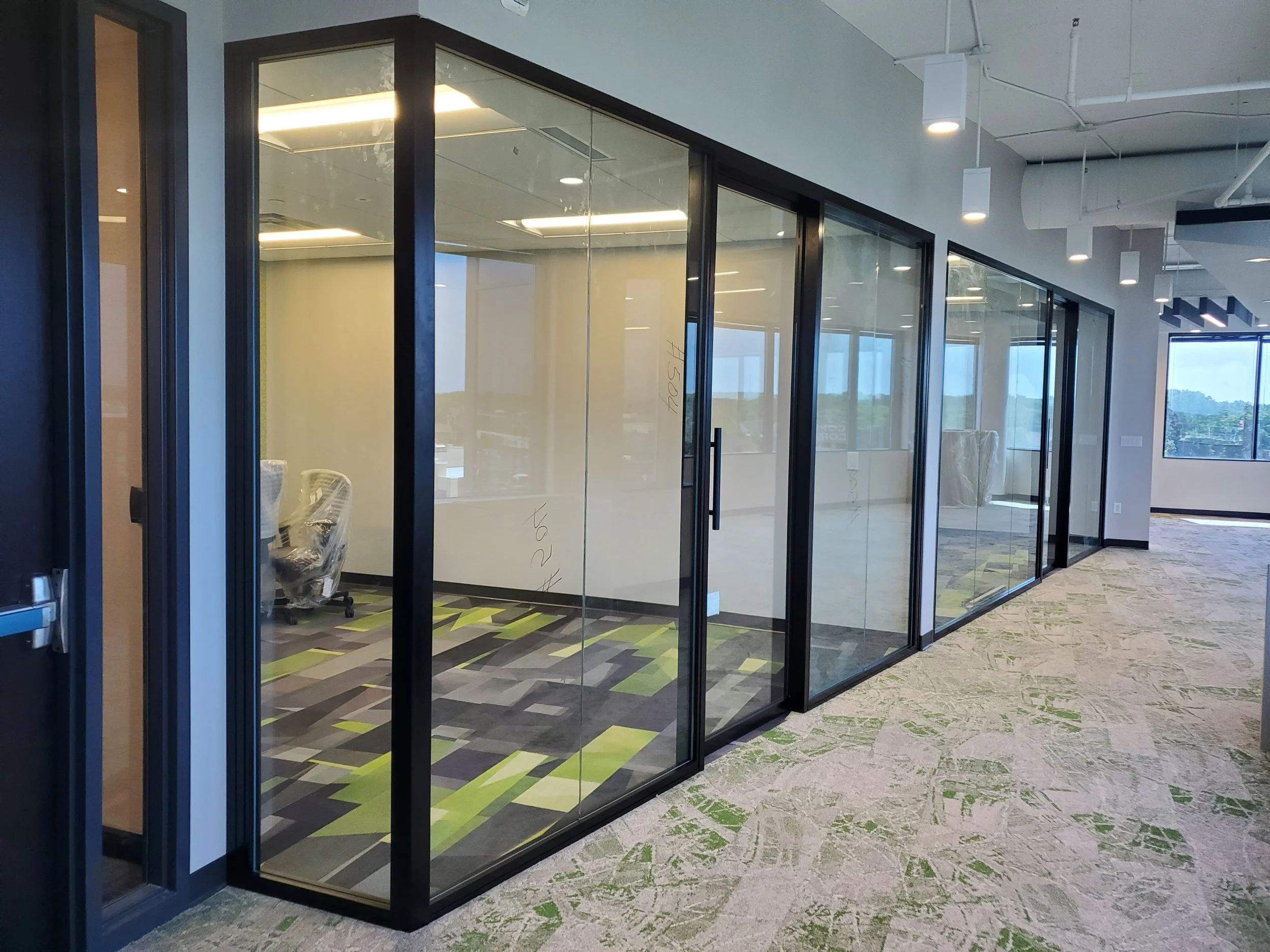 Empty modern office conference room or workspace with glass walls, sliding glass doors, and ceiling lights, view from the corridor.