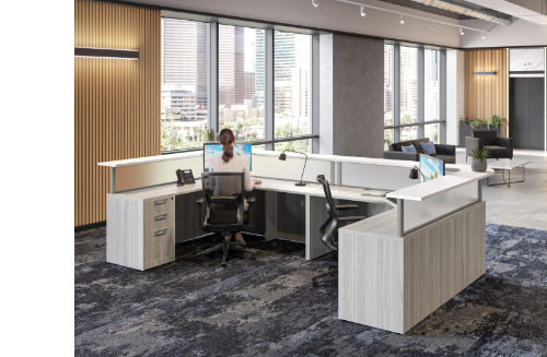 Office with a woman sitting at a desk in front of large windows with city view, modern furniture, and a gray and wood interior.