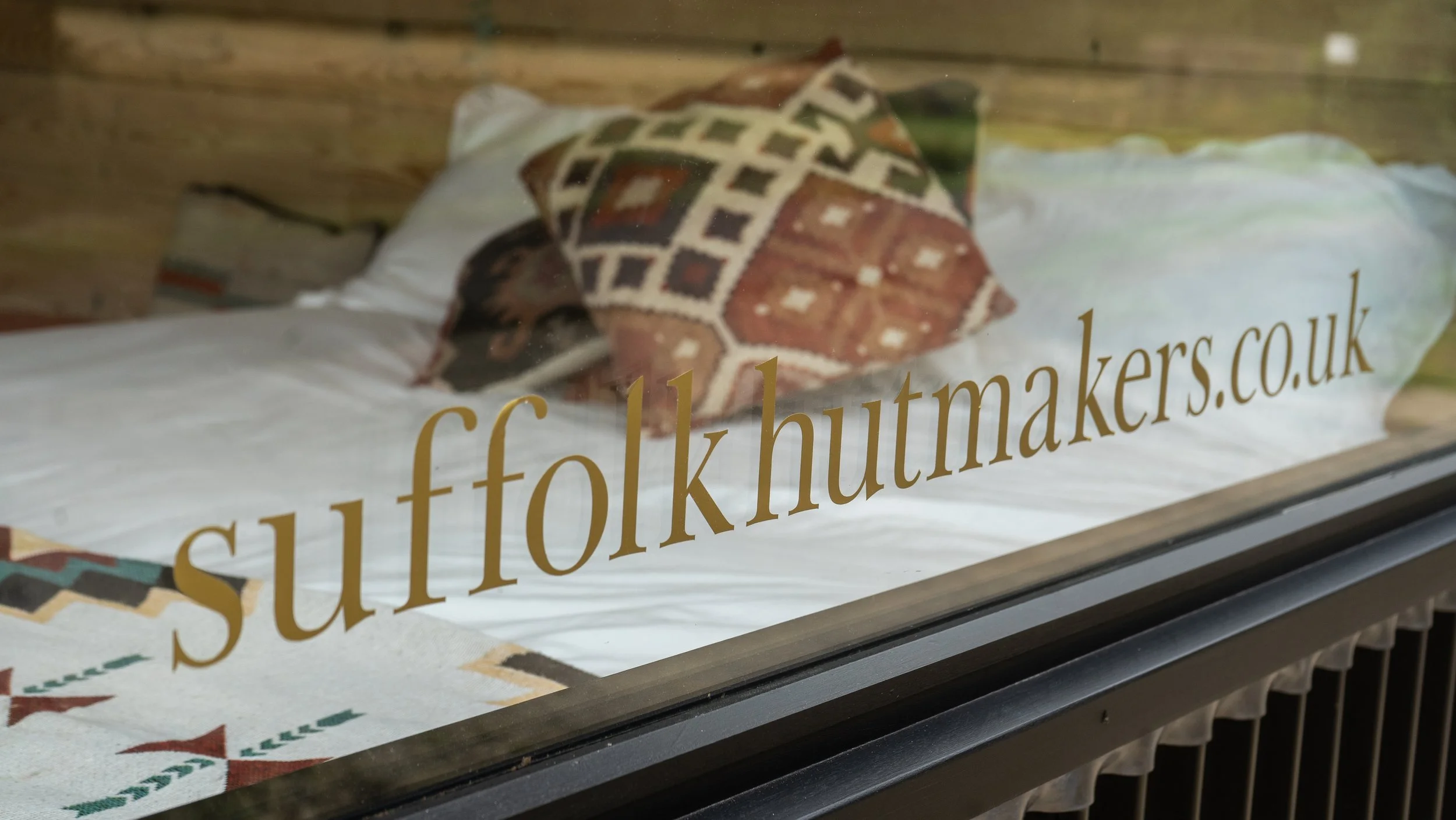 A packaged knitted item with a geometric pattern in earth tones, viewed through a glass window with a website URL printed on it.
