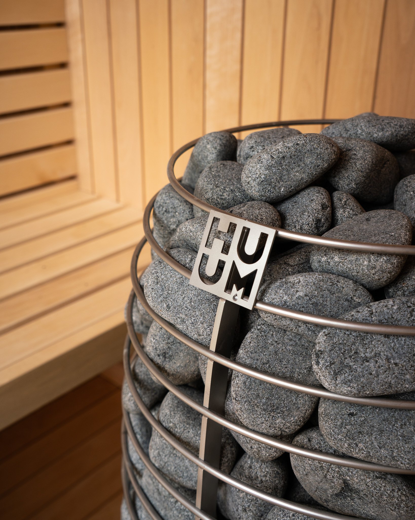 A close-up of a metal container filled with smooth dark stones, with a wooden wall background.