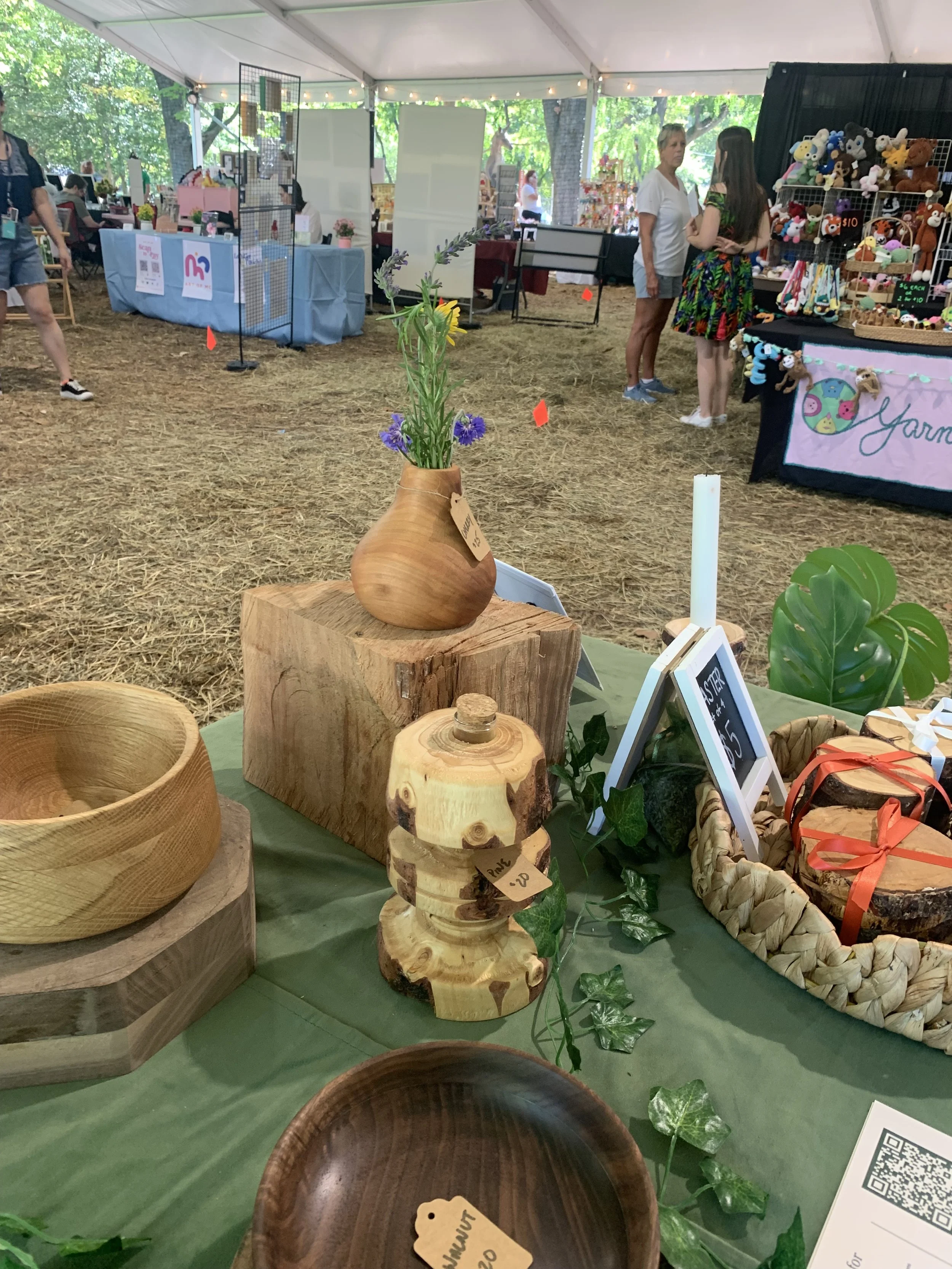 Assorted market goods on a table, highlighting a cherry vase with flowers inside