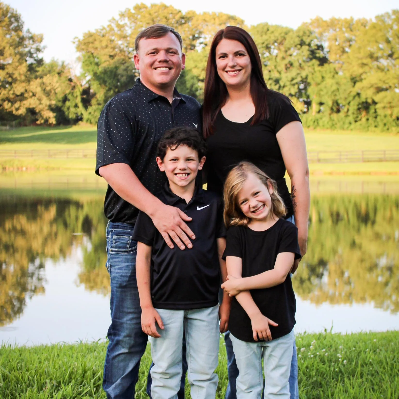 Family of five standing by a lake with trees in the background, smiling at the camera.