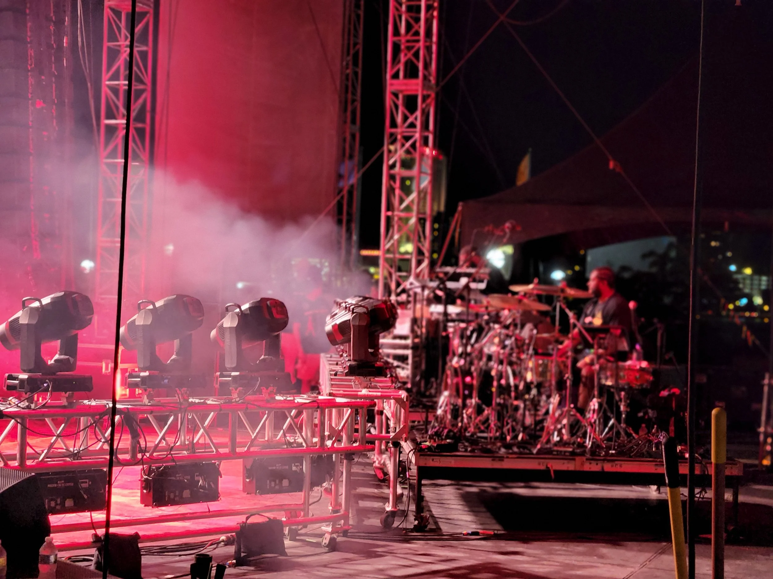 Stage with lighting and equipment, red stage lights, scaffolding, smoke, and a person standing on the right side.