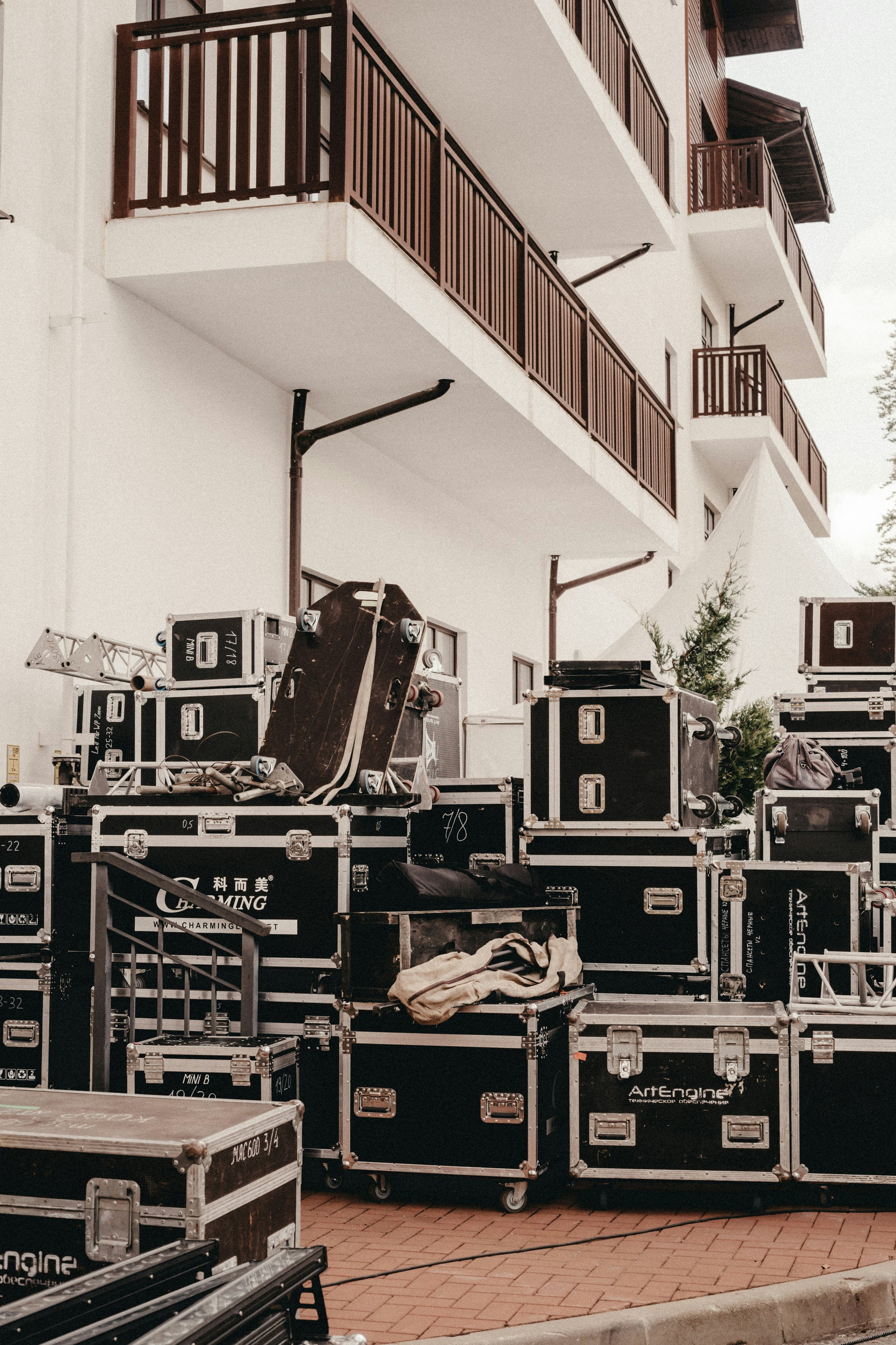 Equipment and cases stacked up outside a building with white walls and brown balconies.