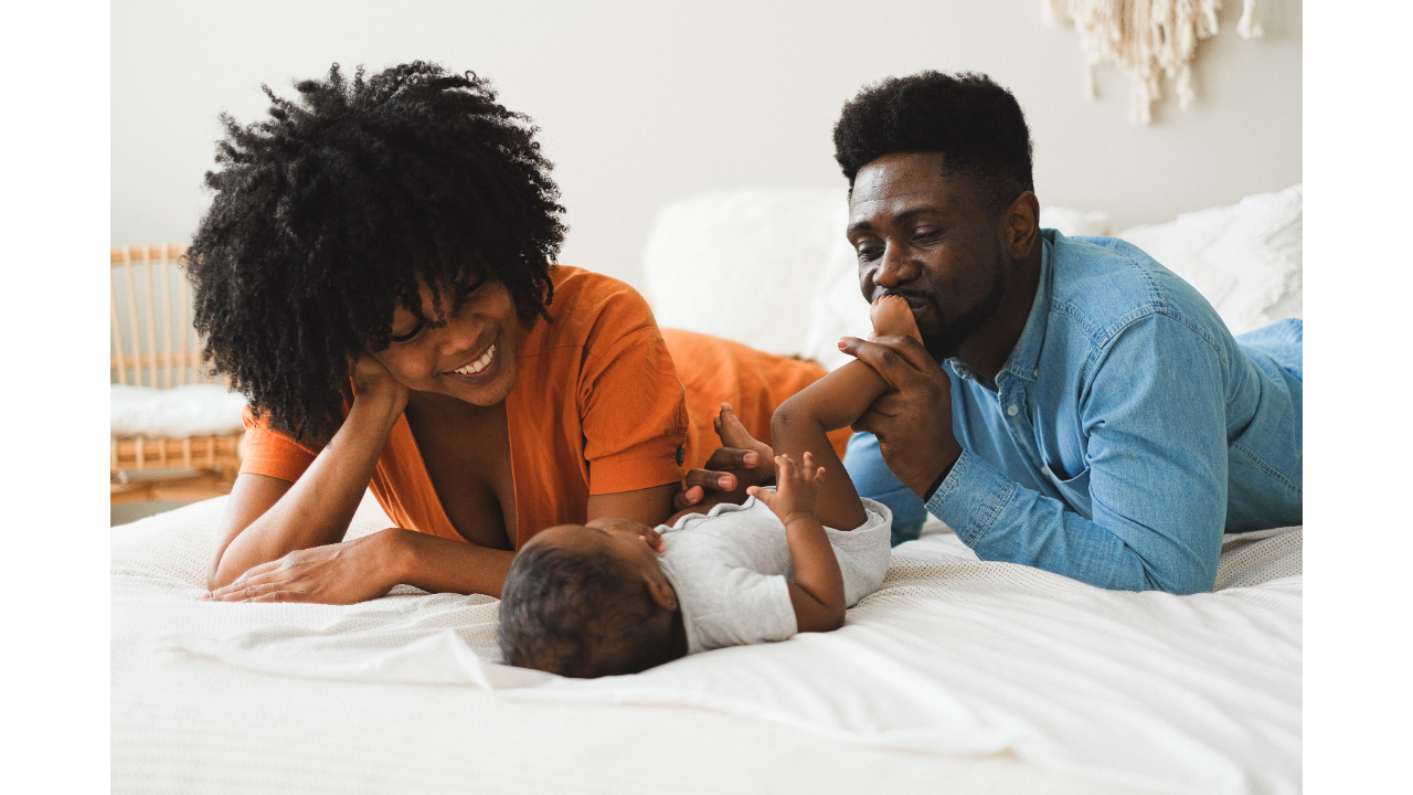 A happy family with a mother, father, and infant lying on a bed together in a bedroom.