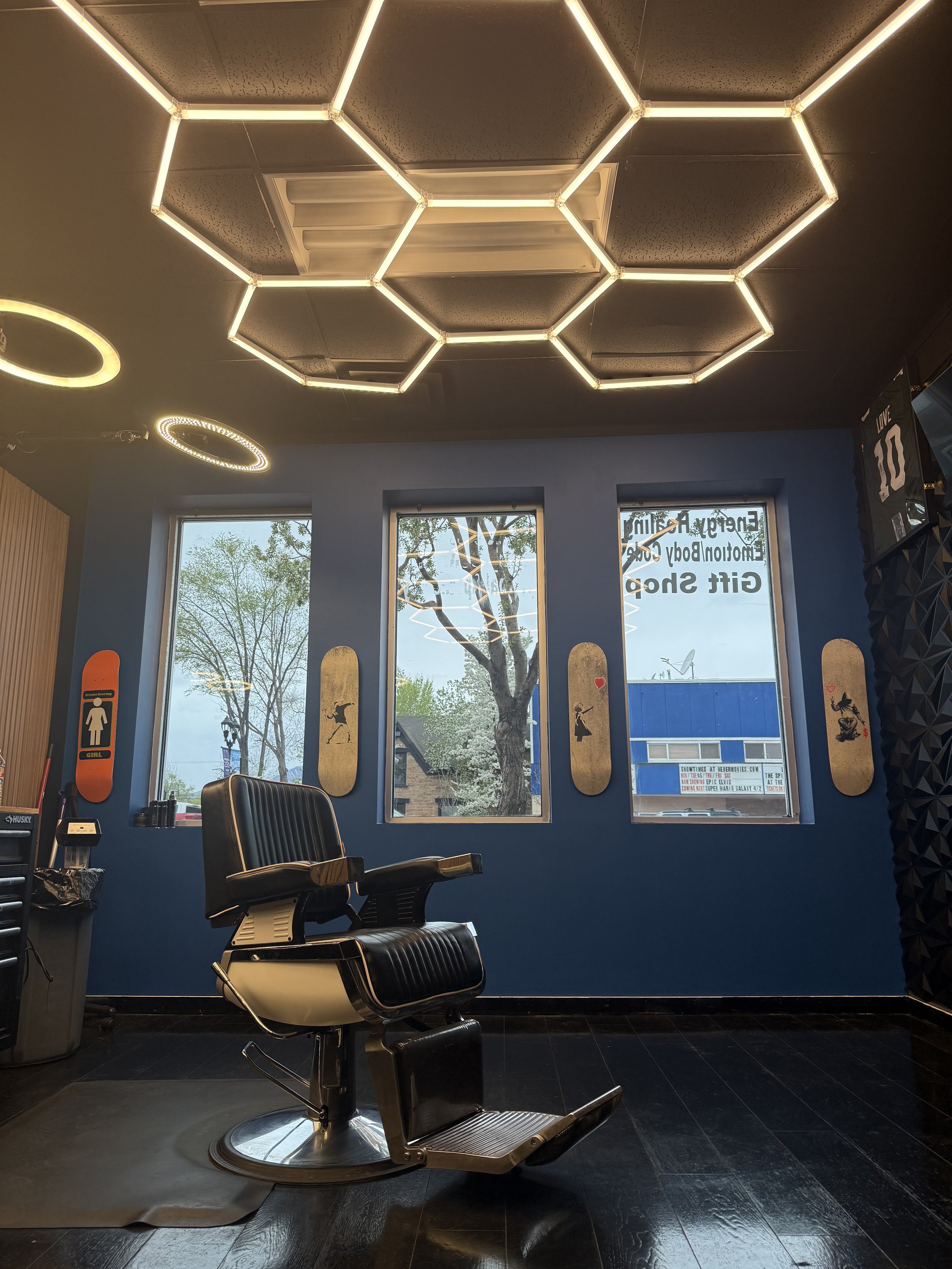 Interior of a barbershop with a black barber chair, three large windows, and a modern hexagonal LED ceiling light fixture.