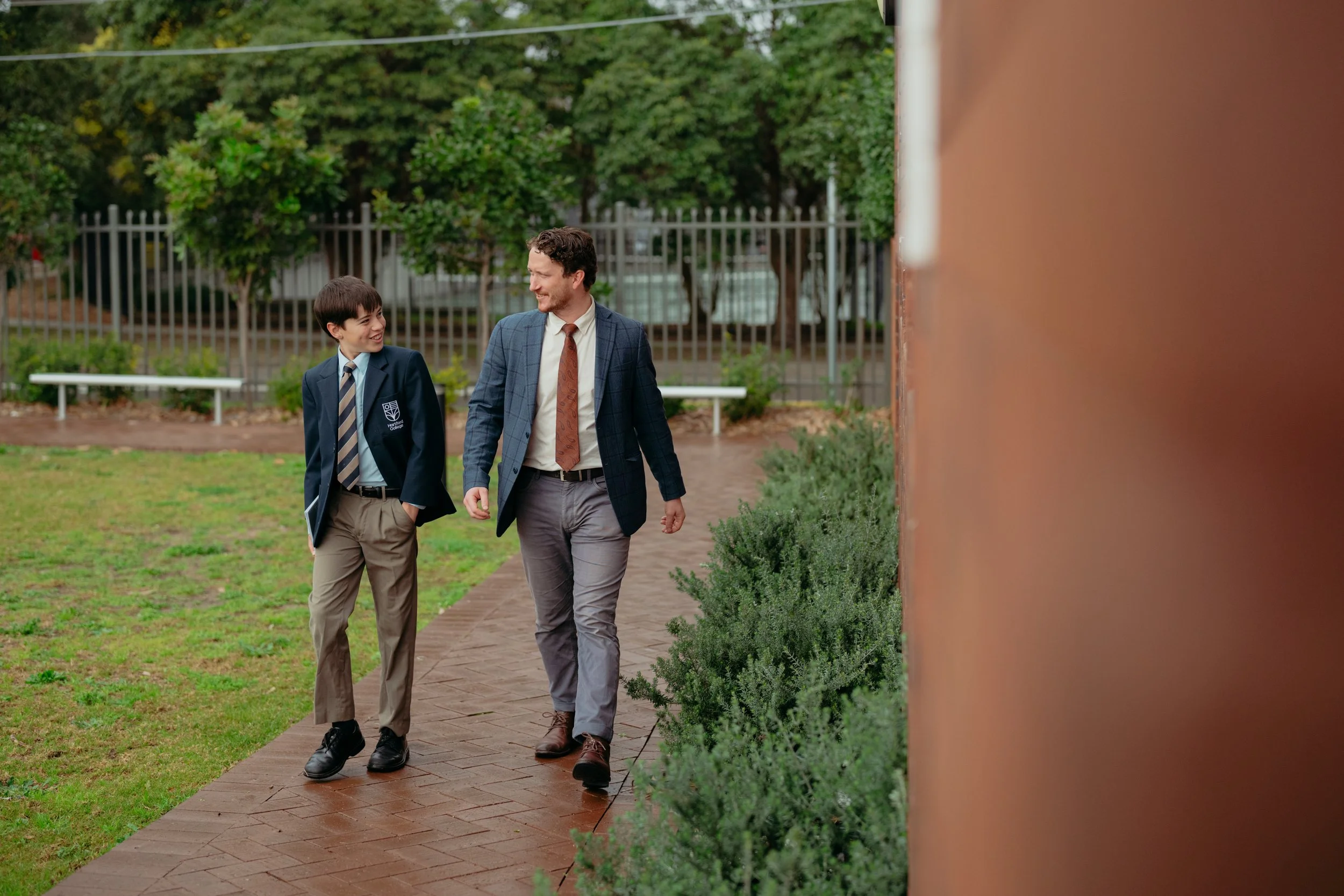 A boy and a teacher sitting outdoors, engaging in conversation and laughing, with greenery and trees in the background.