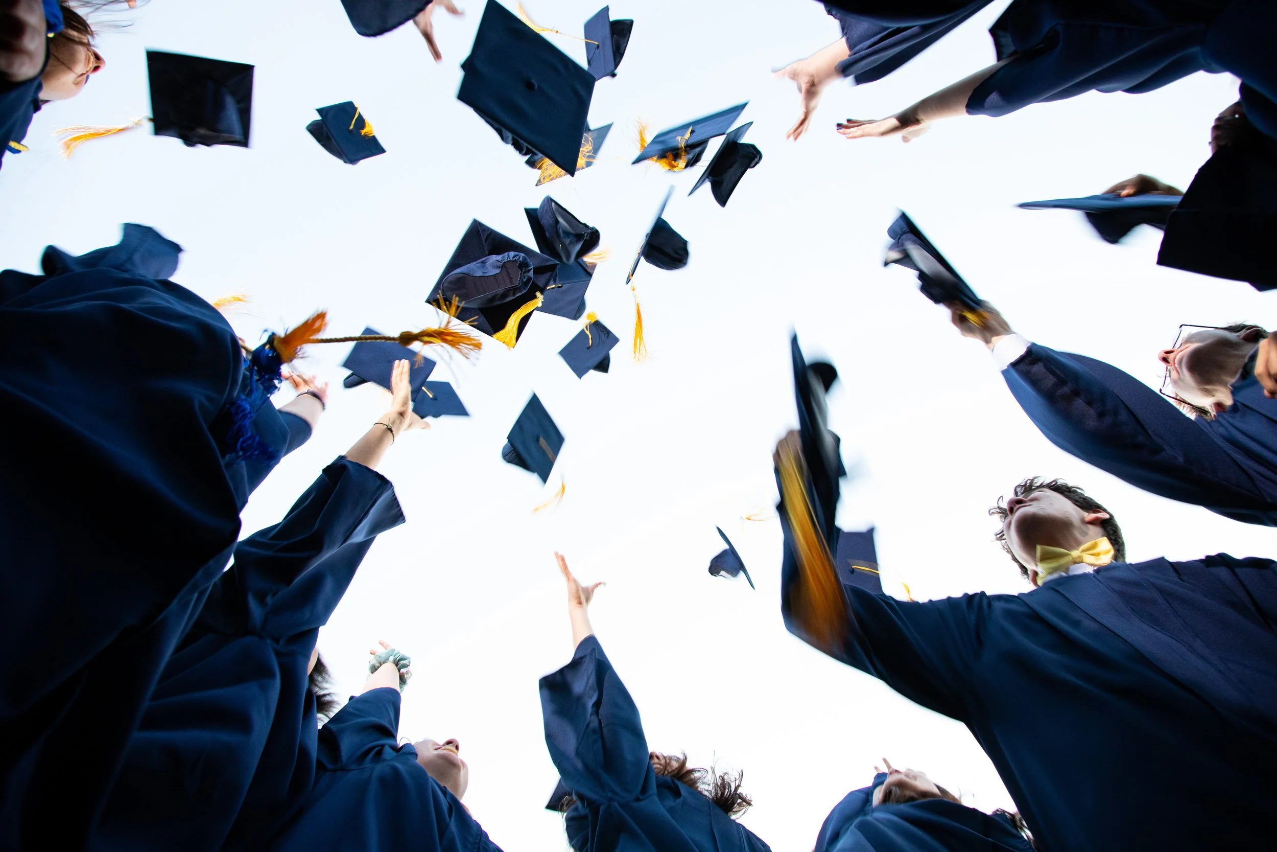Group of graduates in caps and gowns throwing their caps into the air during a graduation celebration.