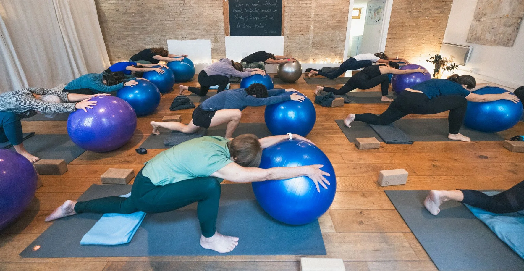 Groupe de personnes participant à un cours de yoga avec des ballons d'exercice dans une salle au sol en bois. Happy Shala Studio Yoga Pilates Grenoble