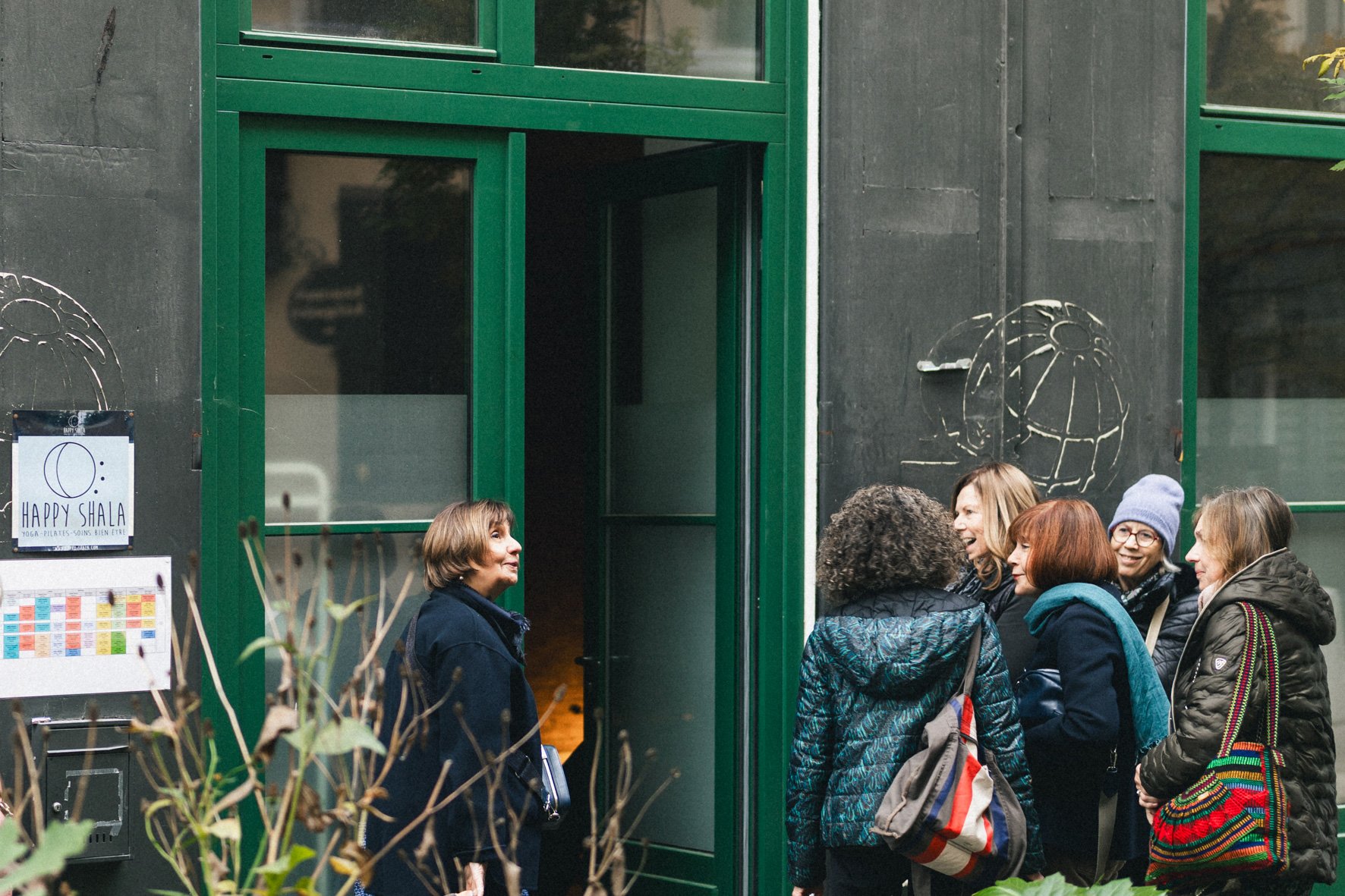 Groupe de personnes bavardant à la sortie d'un bâtiment avec une façade verte, lors d'une réunion ou d'un événement convivial. Happy Shala Studio Yoga Pilates Grenoble