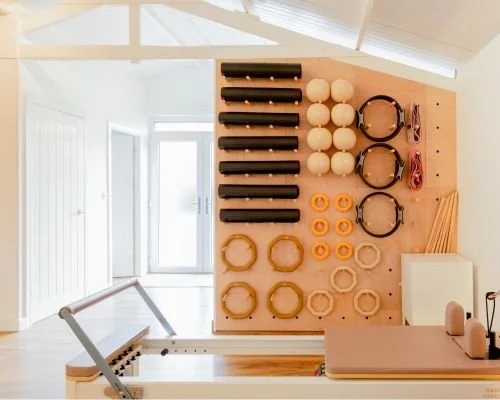 Wall-mounted organizer with Pilates equipment and weights in a well-lit studio.