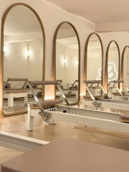 Fitness studio with Pilates reformer machines and large mirrors along the wall.