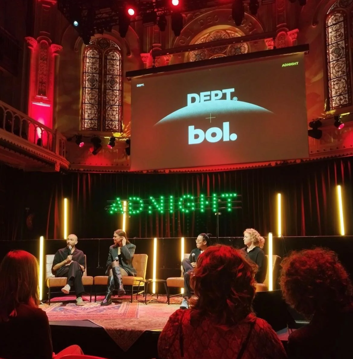 A panel discussion on stage at Paradiso Amsterdam, at a conference called ADNIGHT, with four people seated with microphones, a large screen displaying 'DEPT + bol.'.