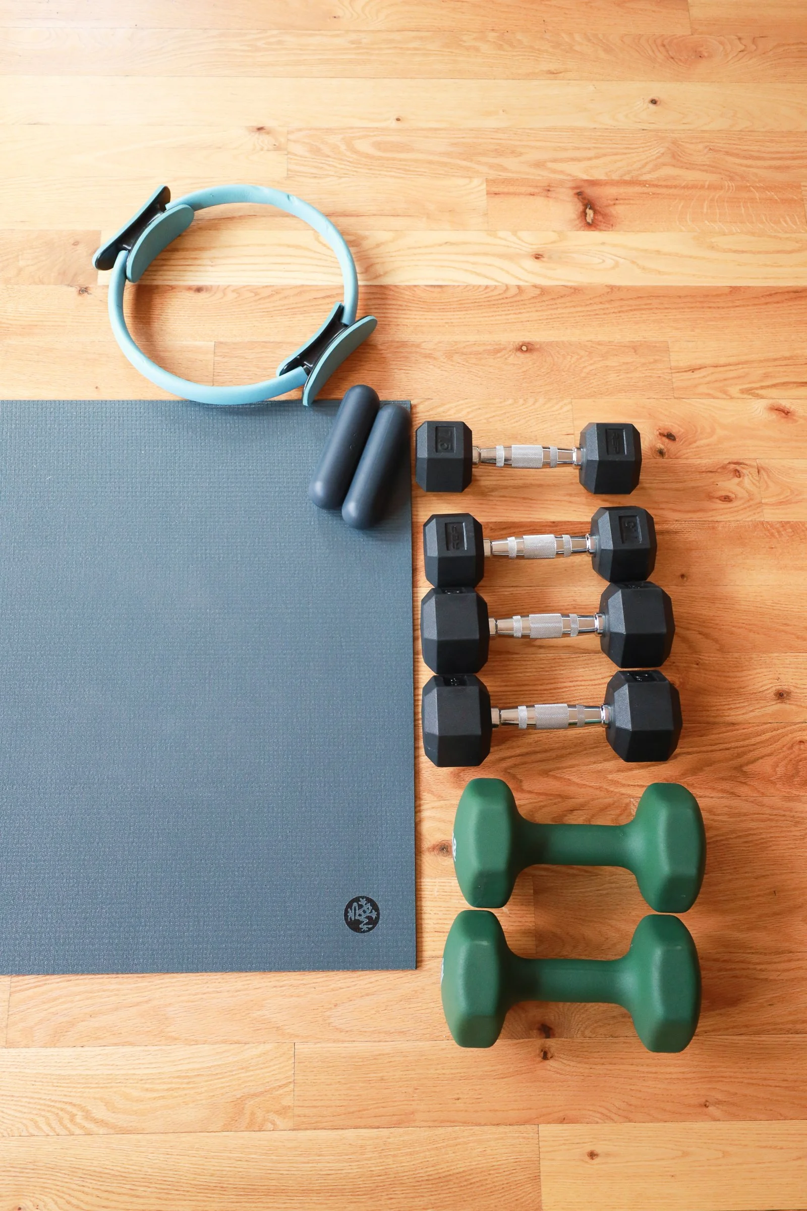 Range Yoga exercise setup including a yoga mat, resistance band, dumbbells, kettlebells, and a green exercise weight on a wooden floor.