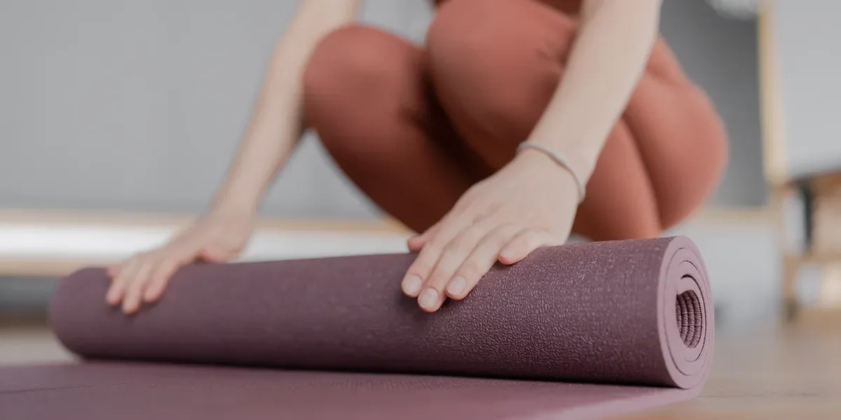 Person in pink leggings unrolling a purple yoga mat on the floor.