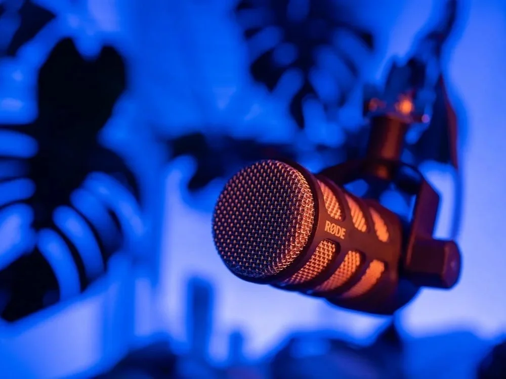 A Rode microphone mounted on a stand in a room with blue lighting.