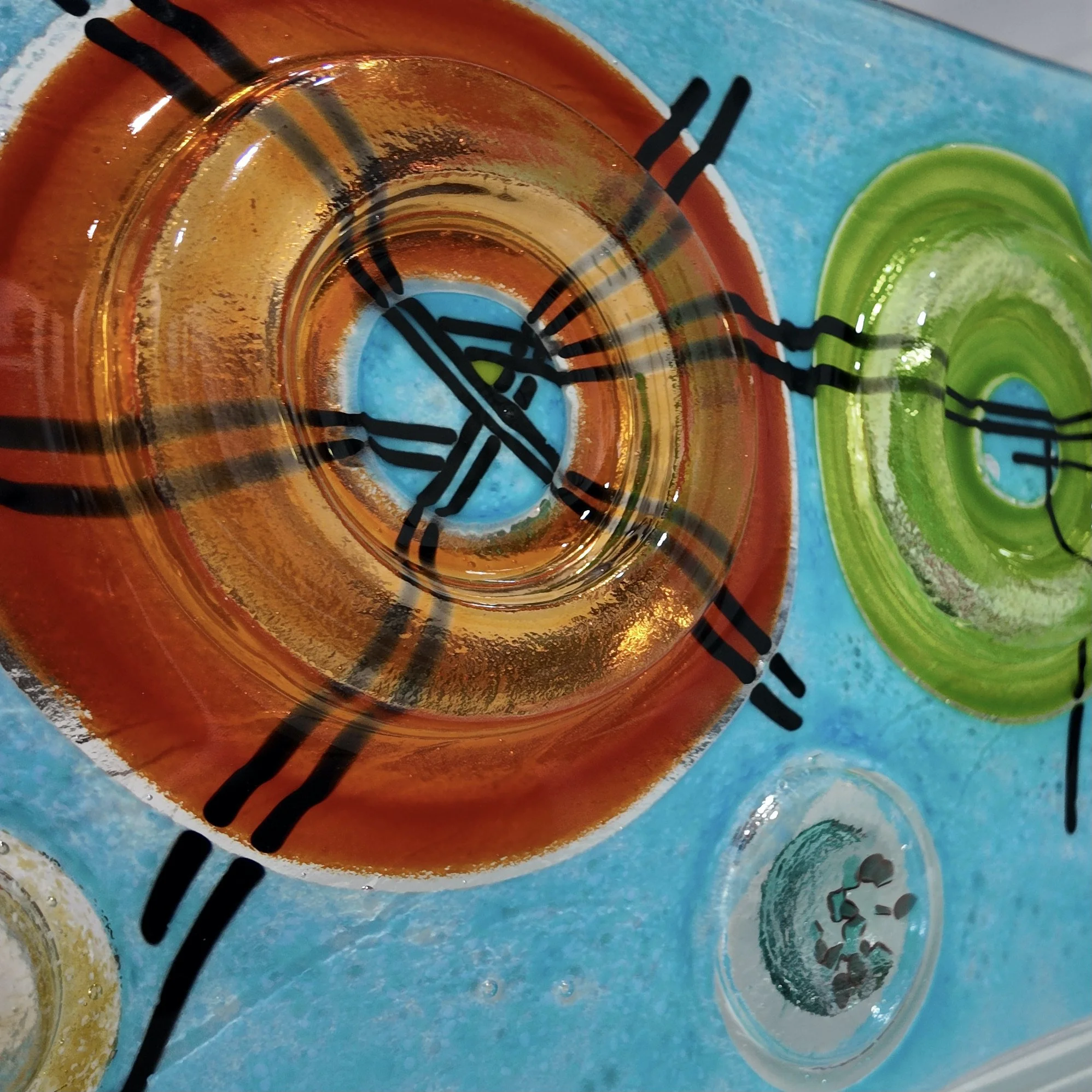 Close-up of orange and green glass 3D rings on a custom fused glass panel.