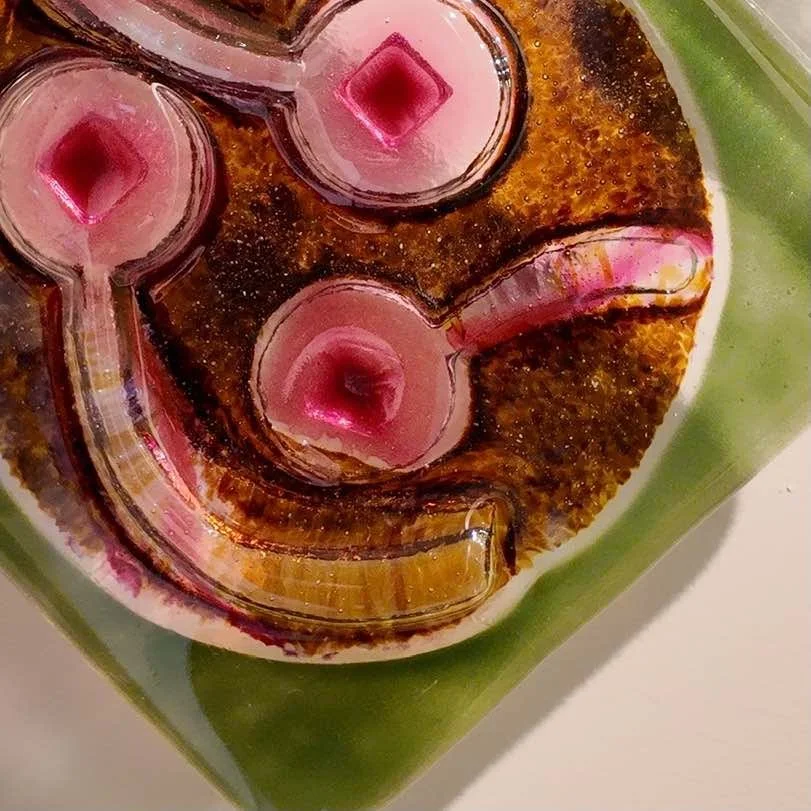 Close-up of a glass candle holder with four pink candles on a green surface.
