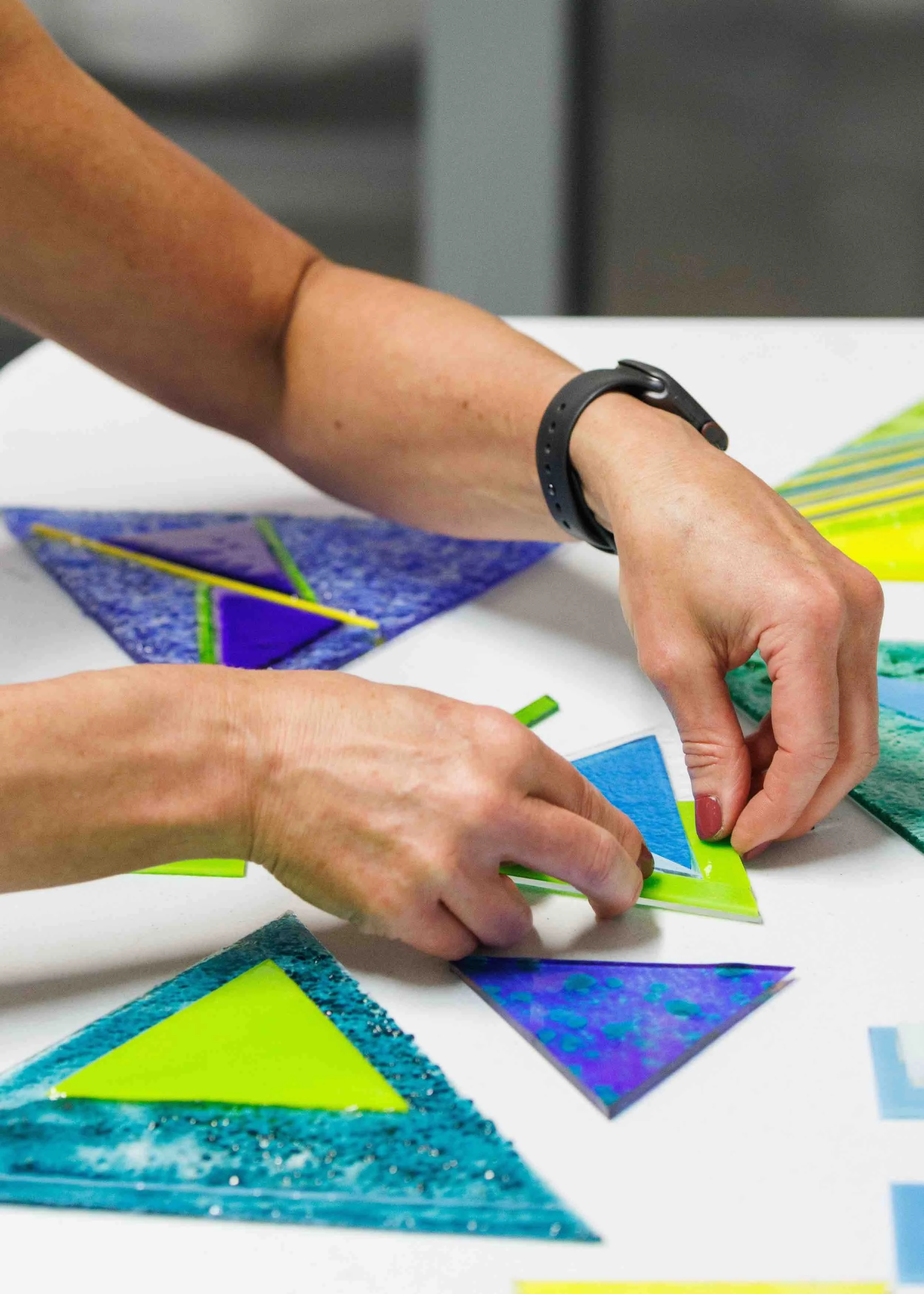Two people working on a colorful geometric art project with various patterned paper and materials on a white table.