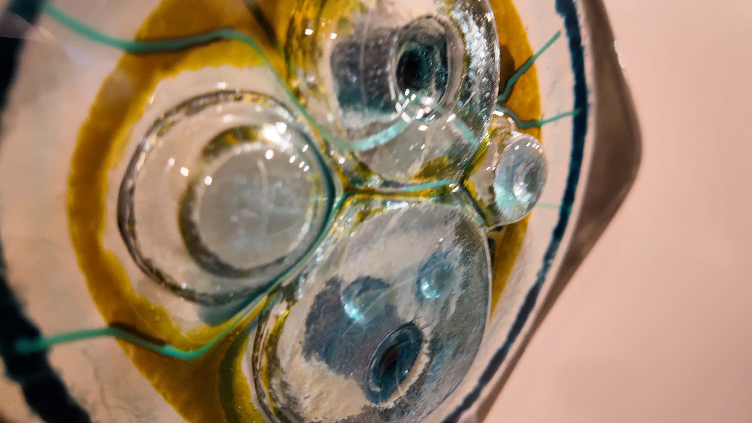 Close-up of a glass object with multiple circular glass circles and colored lines, placed on a surface with yellow, green, and grey borders.