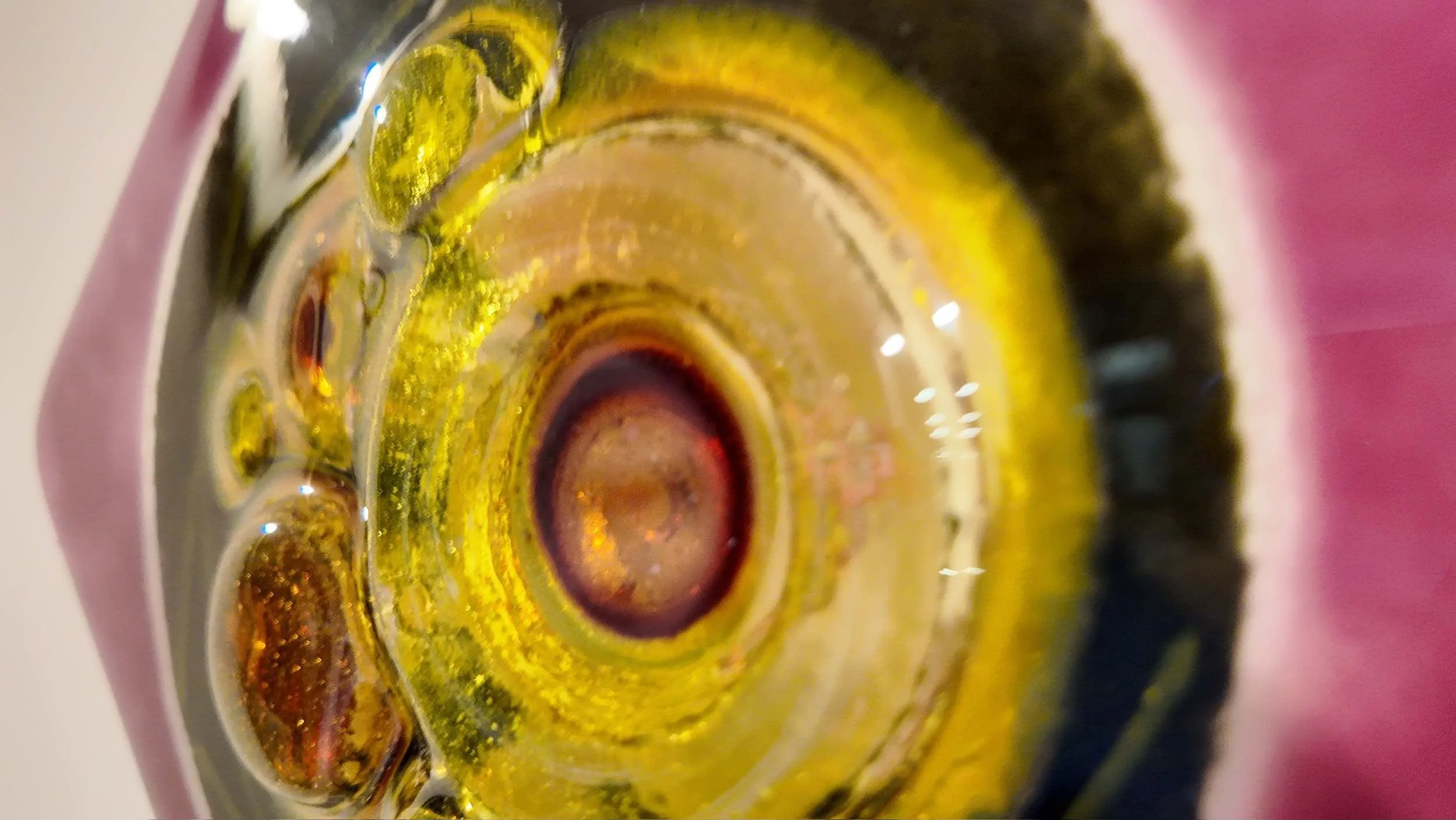 Close-up of a colorful, patterned glass object with marigold and amber  bubbles, with a fuschia border