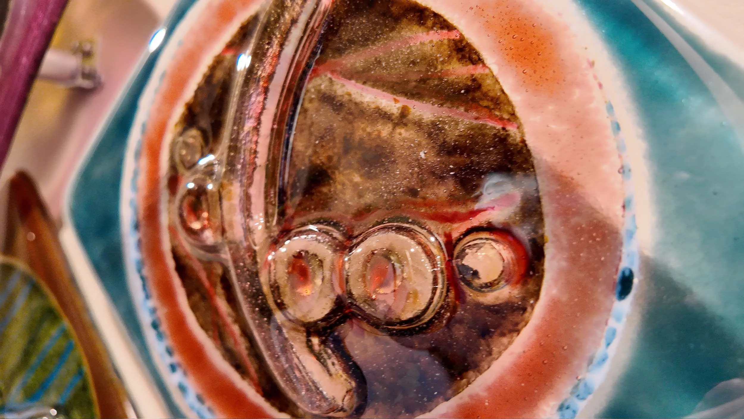 Close-up image of a colorful, patterned glass object with a circular pattern and some sienna and coral spots inside.