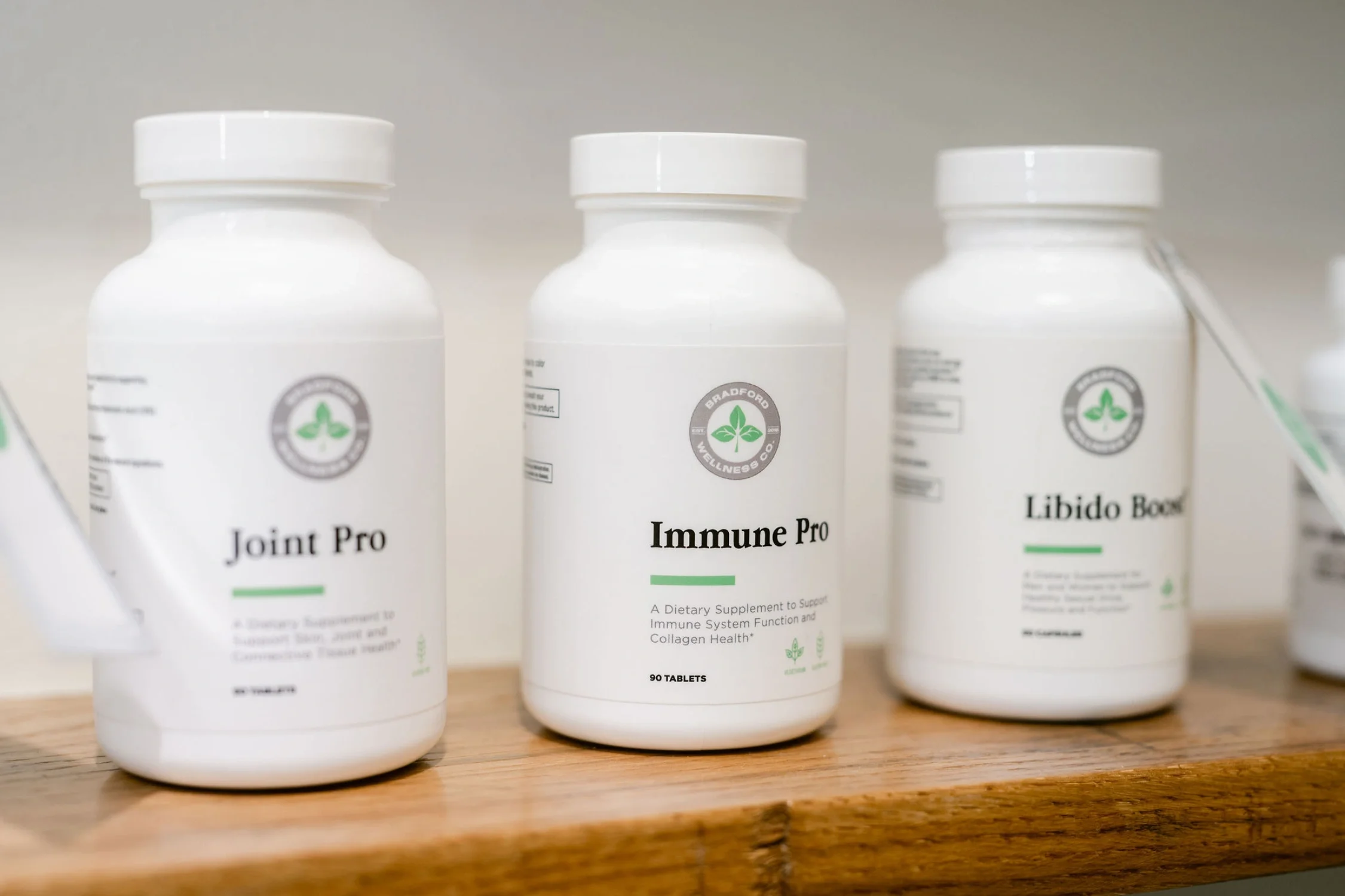 Three white bottles of Chinese herbal medicine s labeled Joint Pro, Immune Pro, and Libido Booster on a wooden surface.