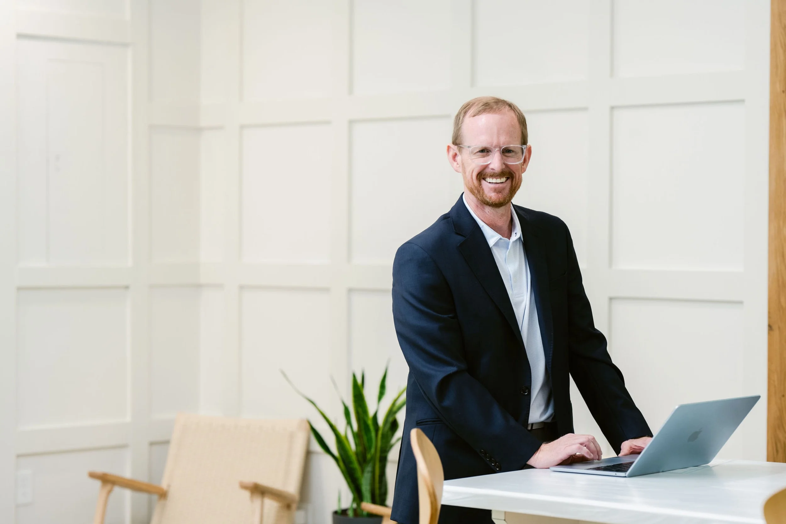 Dr Chad Bradford Scottsboro functional medicine doctor smiling and working on a laptop at a table in a modern, bright office space with white paneled walls, chairs, and a green plant.