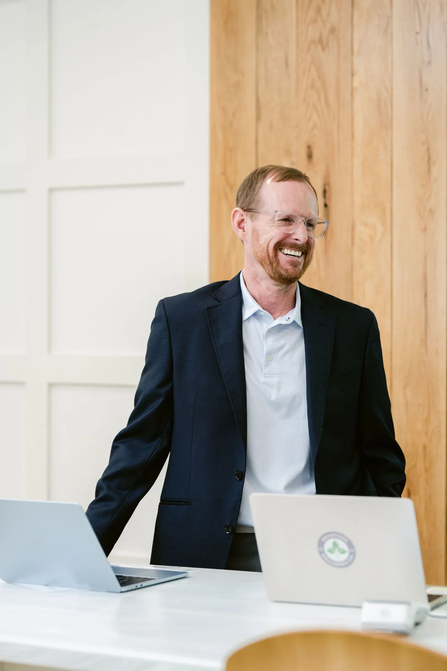 Dr Chad Bradford Scottsboro functional medicine doctor smiling and standing in an office setting with laptops on a white table and wood-paneled wall in the background.