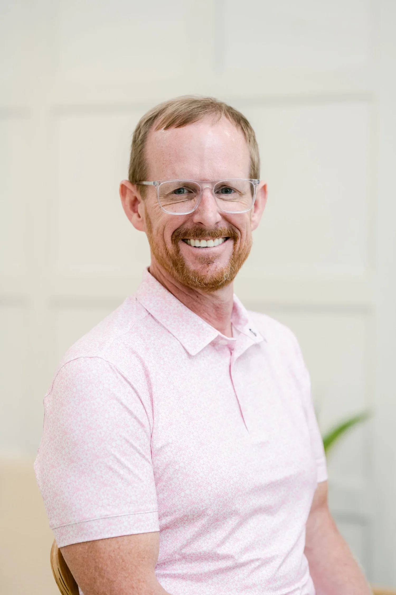 Dr. Chad Bradford wearing a light pink patterned shirt, sitting on a wooden chair in an indoor setting.