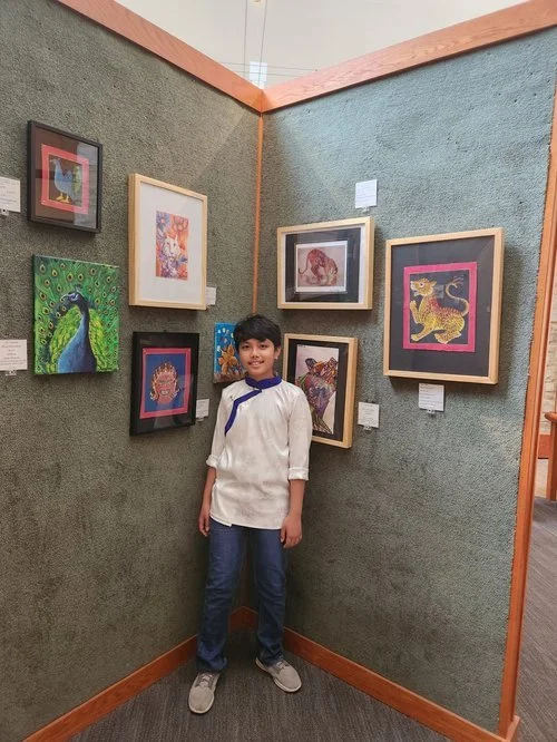 Young artist standing beside a wall of their exhibited work