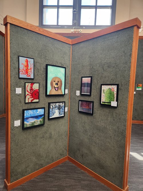 Framed student paintings arranged in rows inside the Riverbend gallery