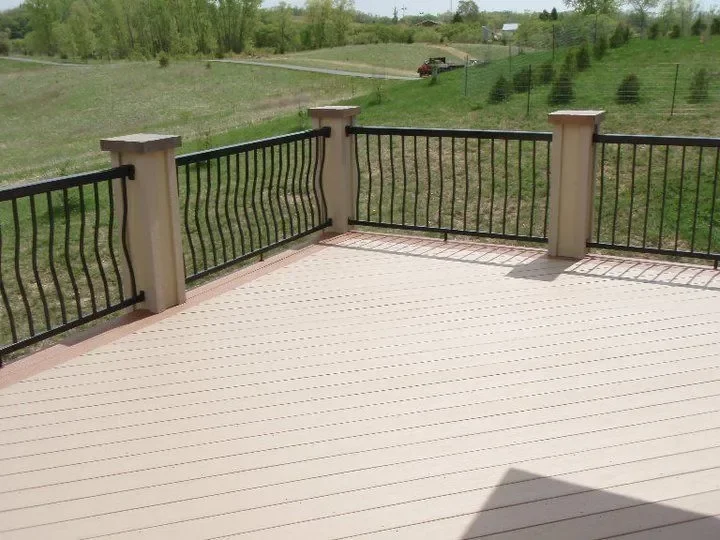Empty outdoor deck with black metal railing, overlooking green fields and trees in the distance.