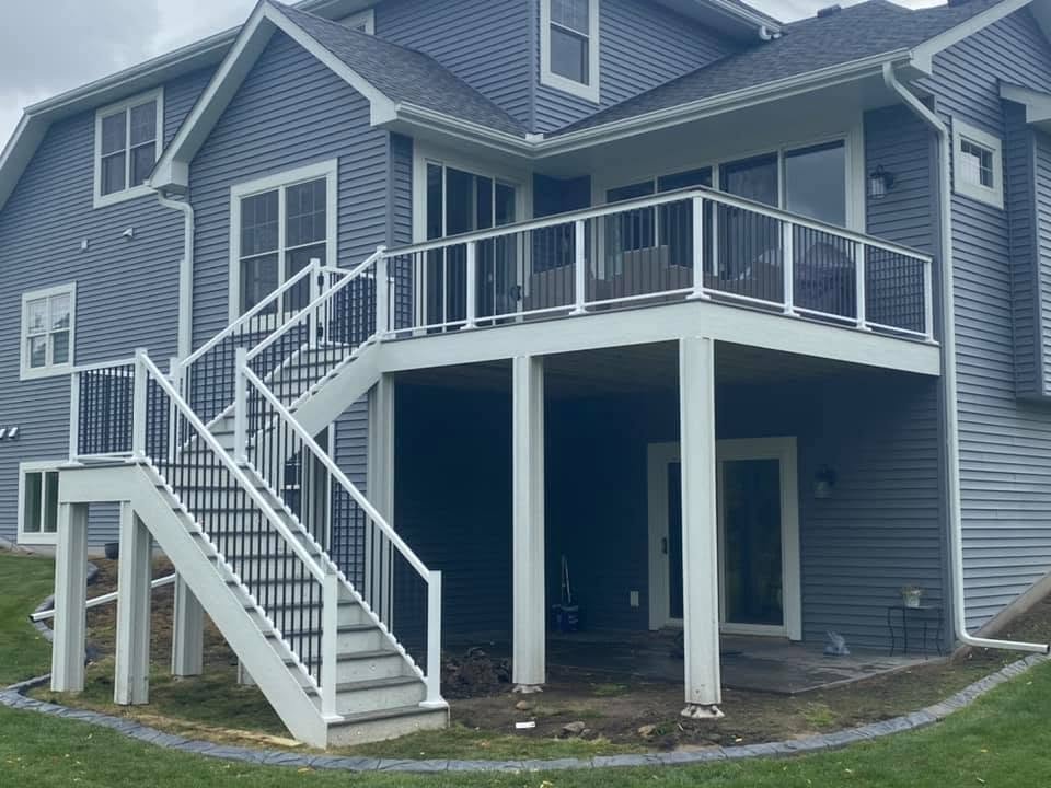 Back view of a blue house with a two-level deck and white railing, with stairs leading from the ground to the upper deck.