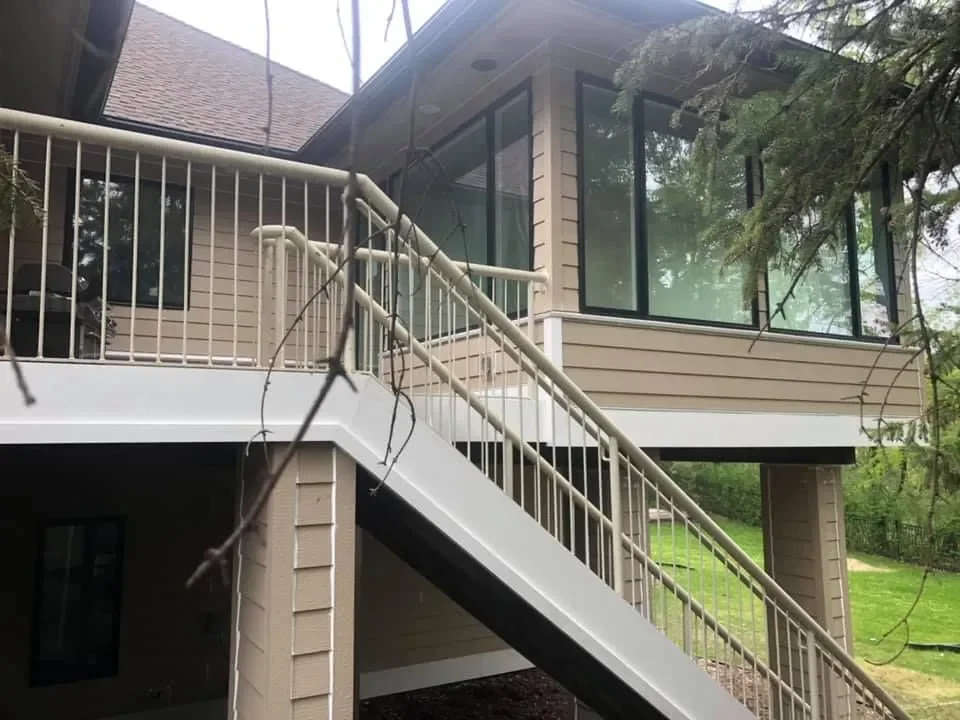A two-story house with large glass windows and an exterior staircase leading to a balcony.