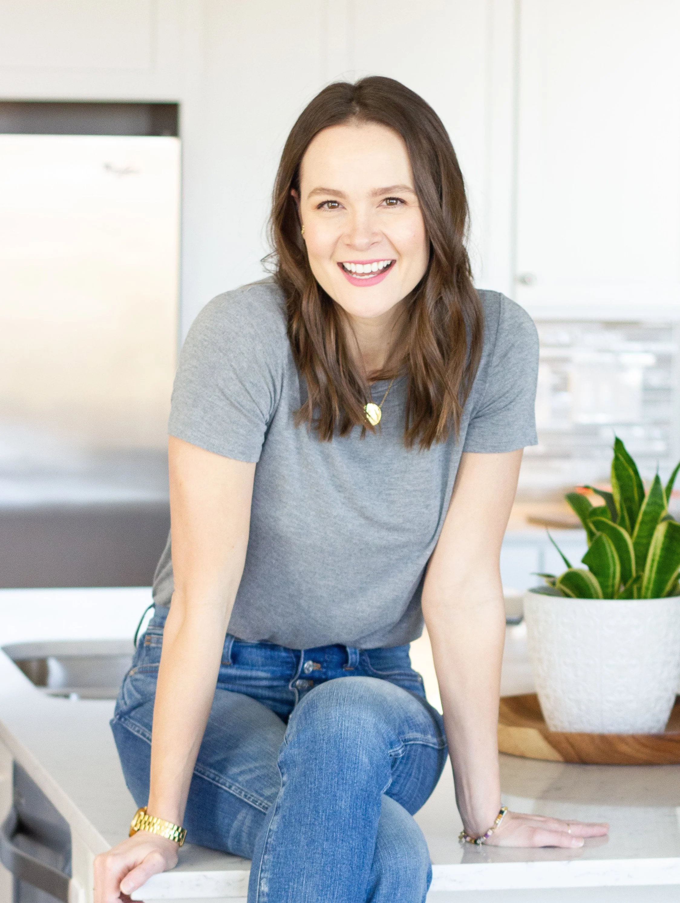 Tara Noseck sitting on a kitchen counter smiling to introduce herself.