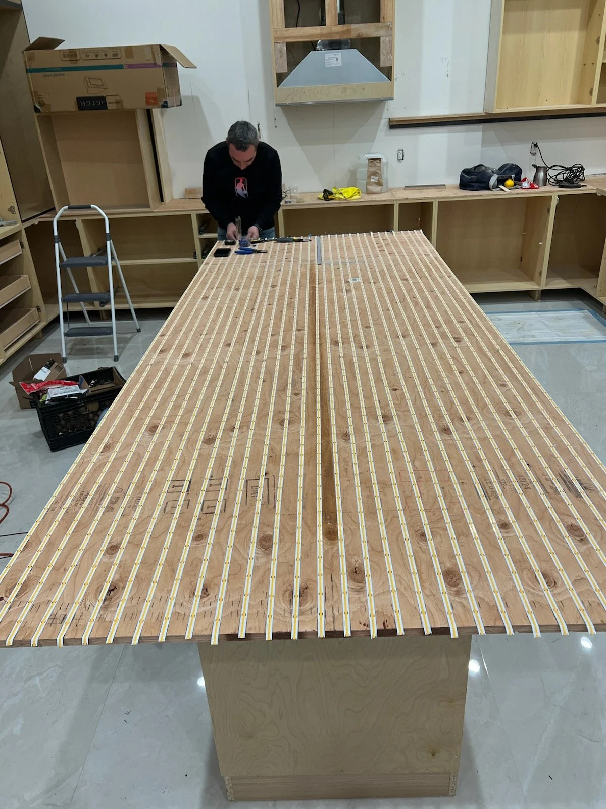 A person working on a large piece of wood with electronic components and LED strips, likely installing lighting.