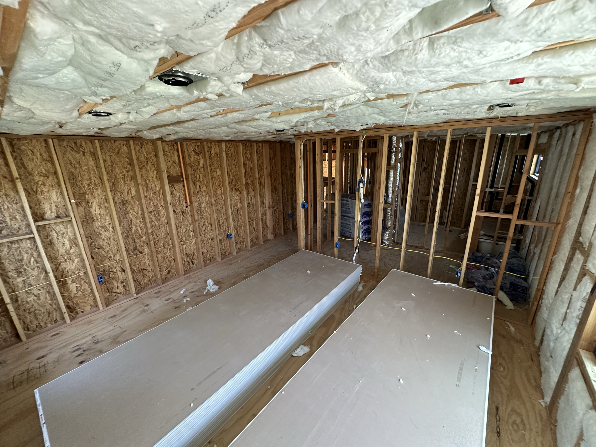 Interior view of a house under construction with exposed wooden framing and insulation panels.