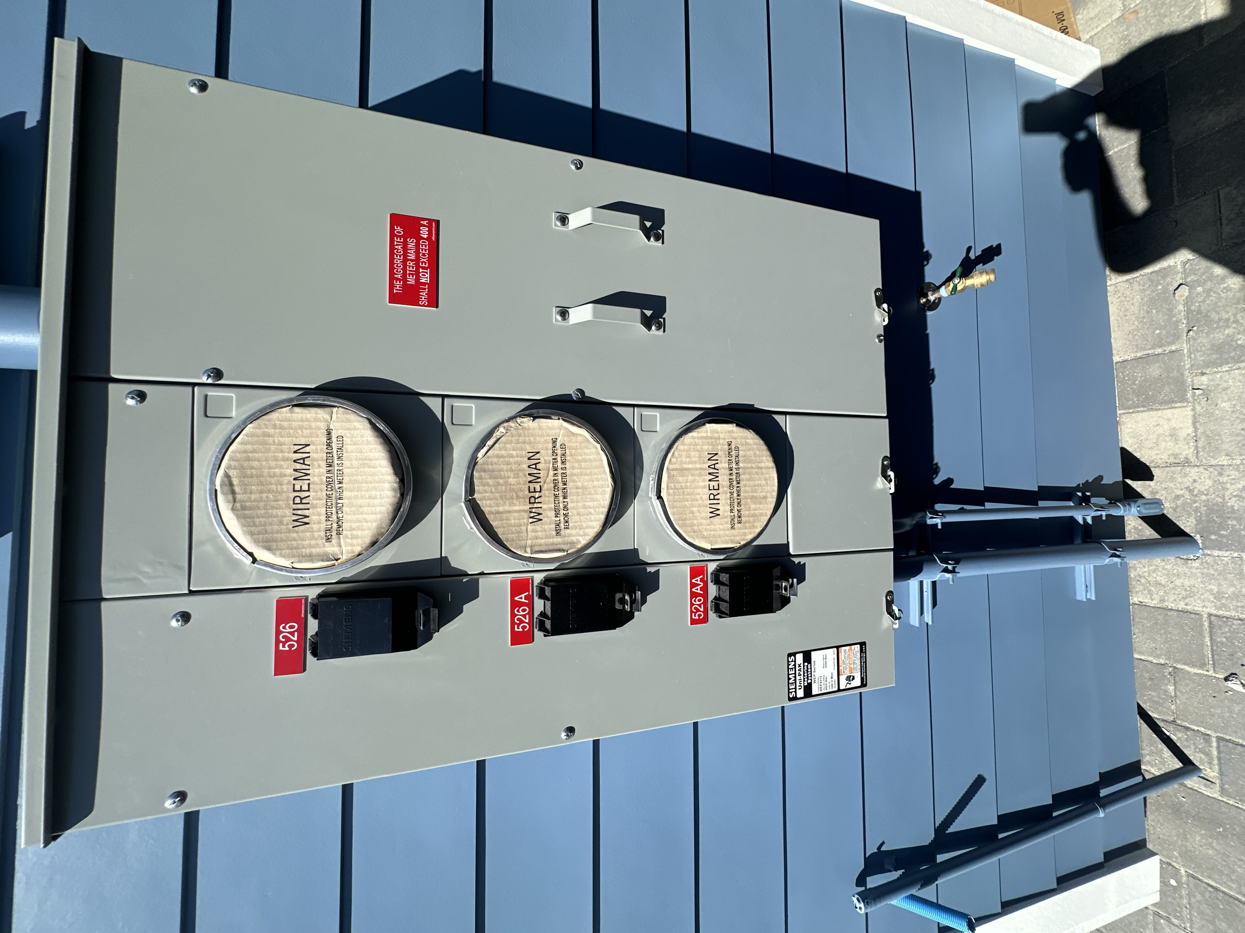 An electrical transformer panel with three large round cover plates labeled 'Wireman' and surrounded by various switches and labels, situated outdoors on a blue surface.