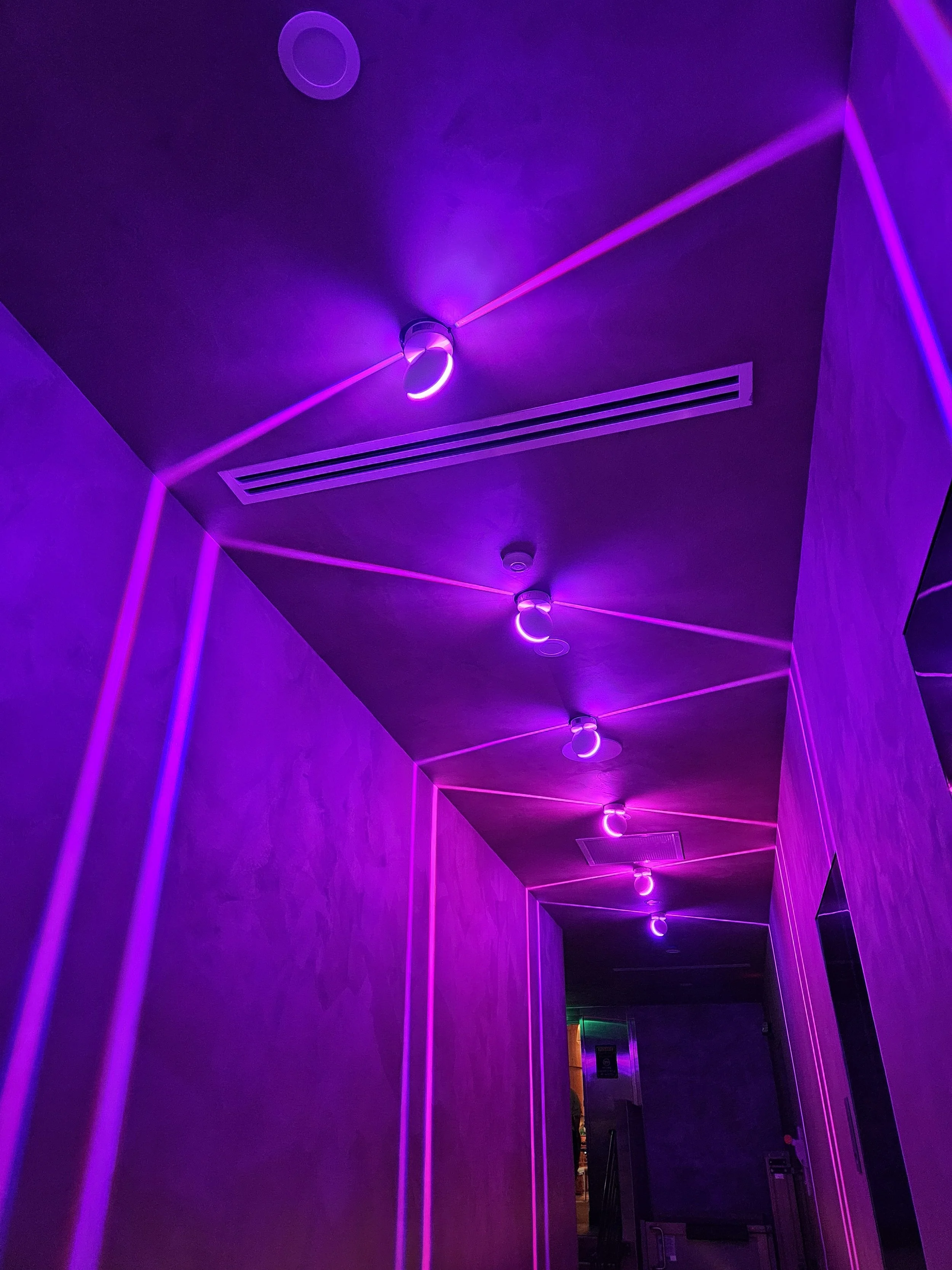 A hallway illuminated with purple and pink LED strip lights on the ceiling and walls.