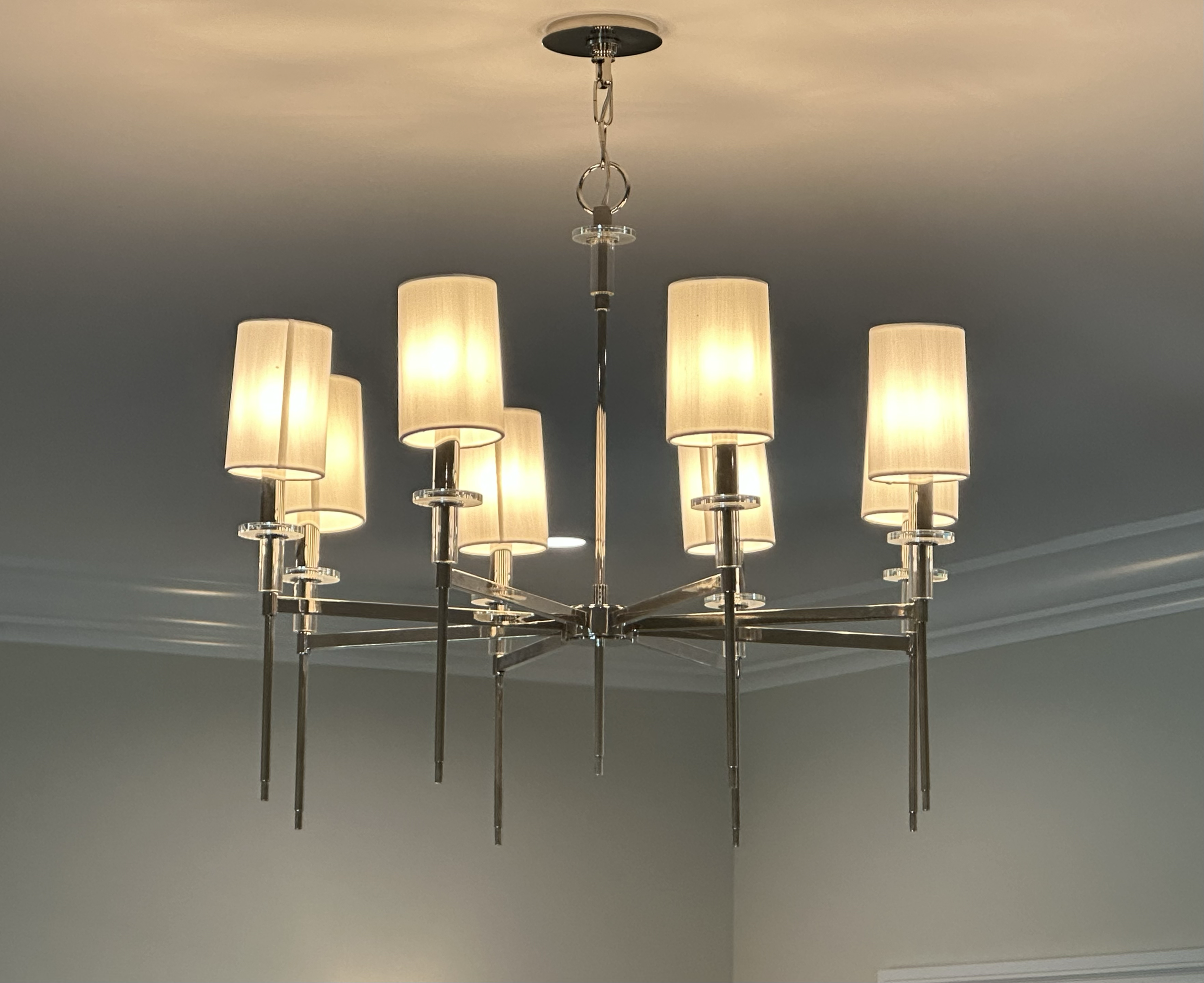 A modern chandelier with multiple cylindrical beige lampshades hanging from a metal fixture, illuminated against a ceiling.