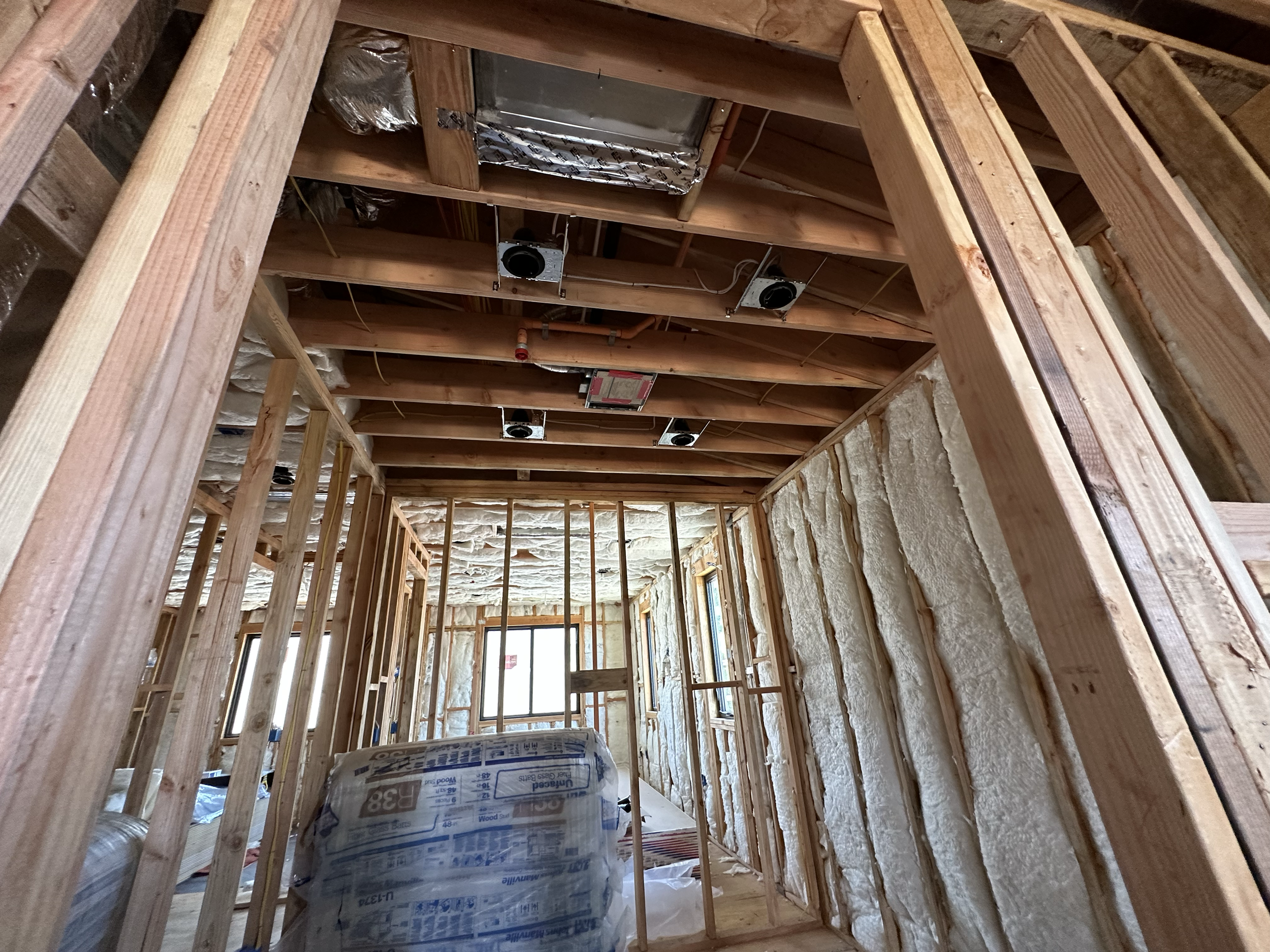 Interior view of a building under construction with exposed wooden framing, insulation, and HVAC ductwork visible on the ceiling.