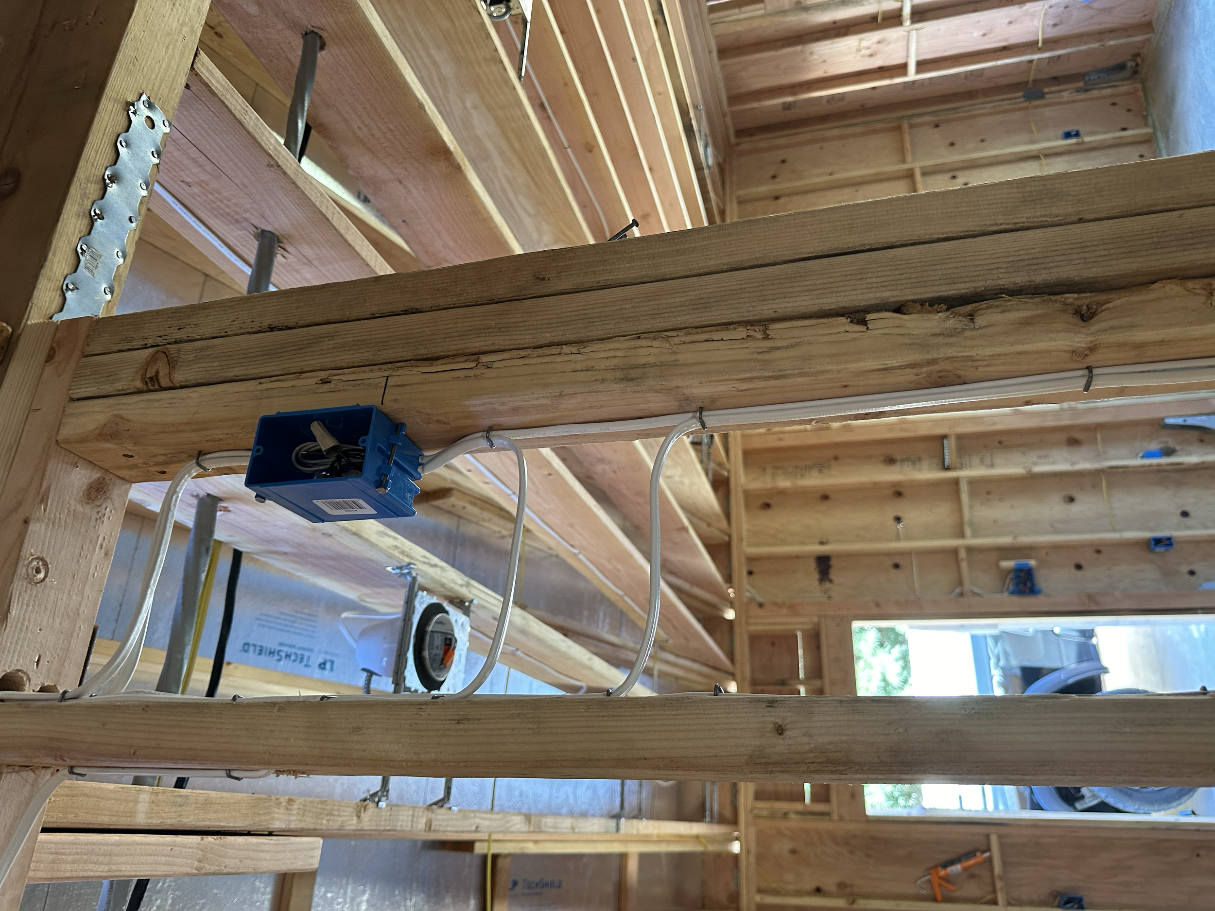 Close-up view of wooden framing during construction with electrical wiring and a blue electrical box installed in a building under construction.