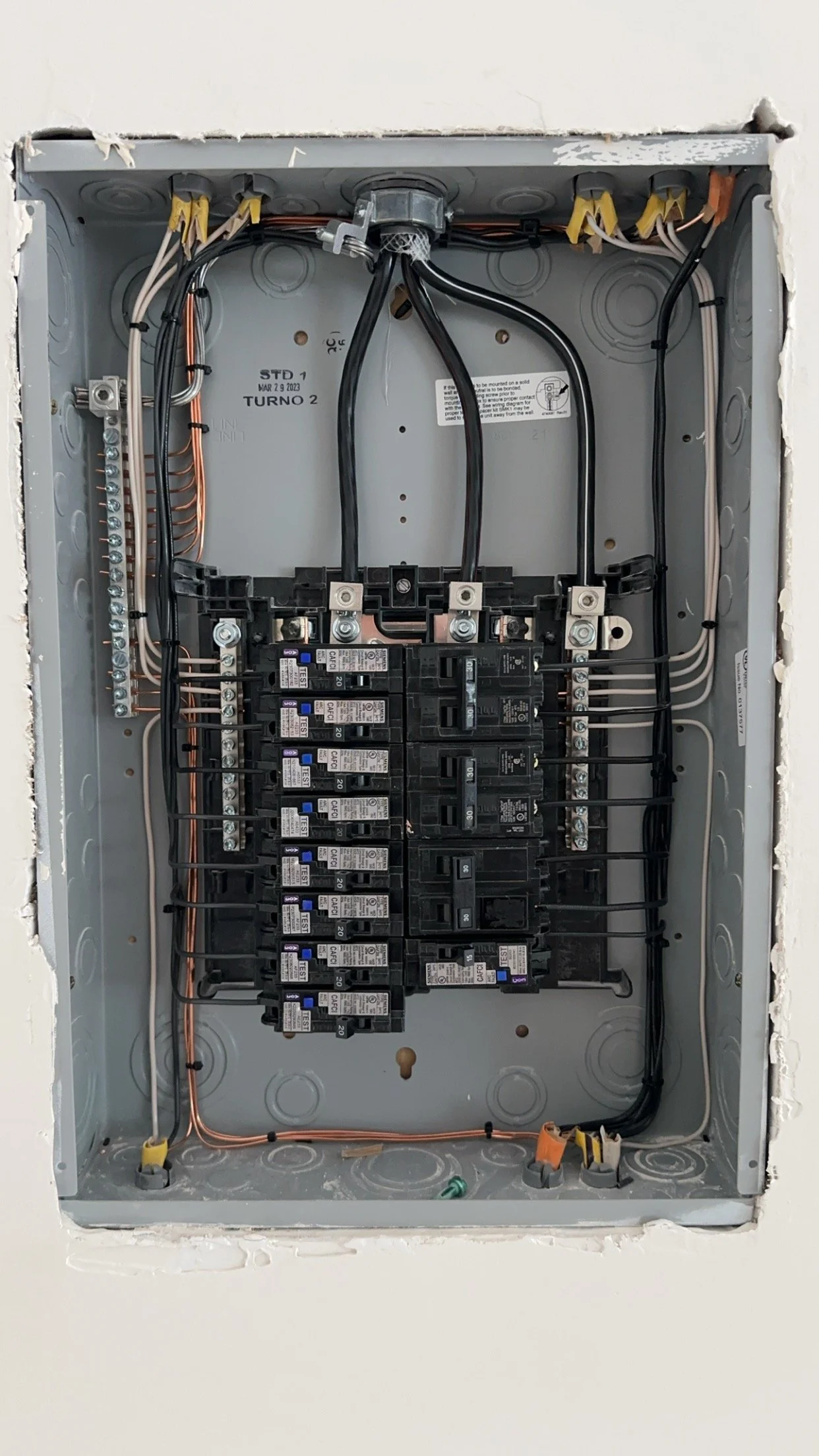 Open electrical breaker box with multiple circuit breakers and wiring inside a gray metal panel.