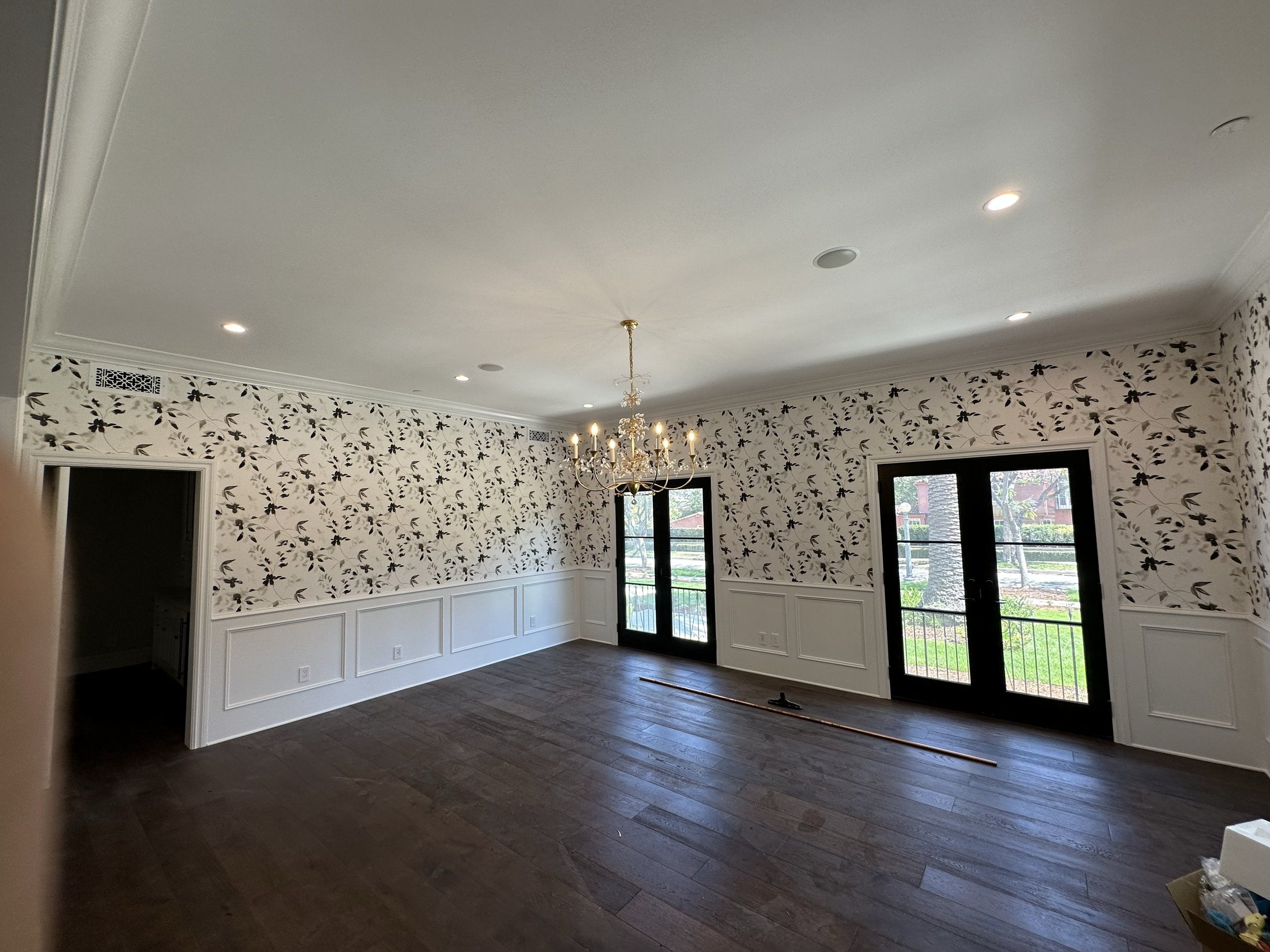 Living room with white ceiling, floral wallpaper, dark hardwood floors, large windows, and a chandelier with lights on.