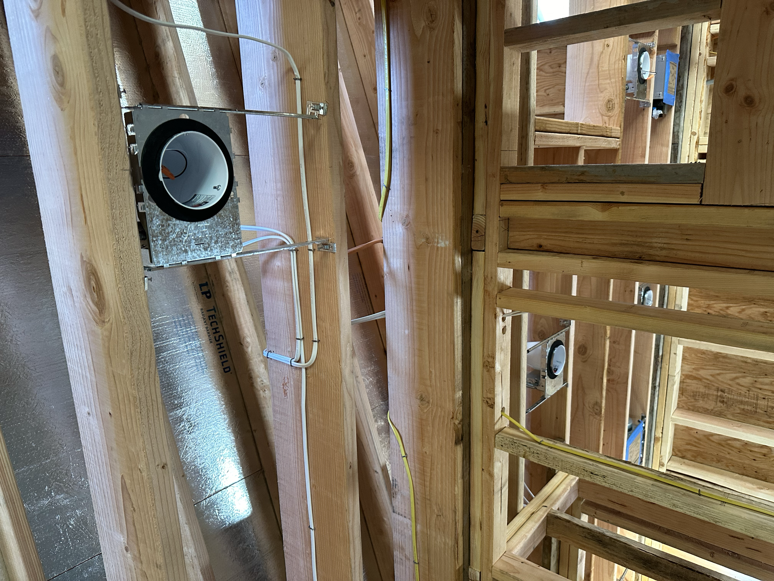 Construction site with wooden framing and electrical wiring, including a metal electrical box with conduit and an electrical outlet.