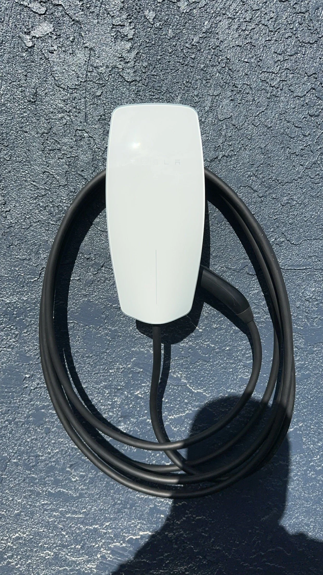 Tesla electric vehicle charging station with a white charging connector and black cable on textured dark pavement.