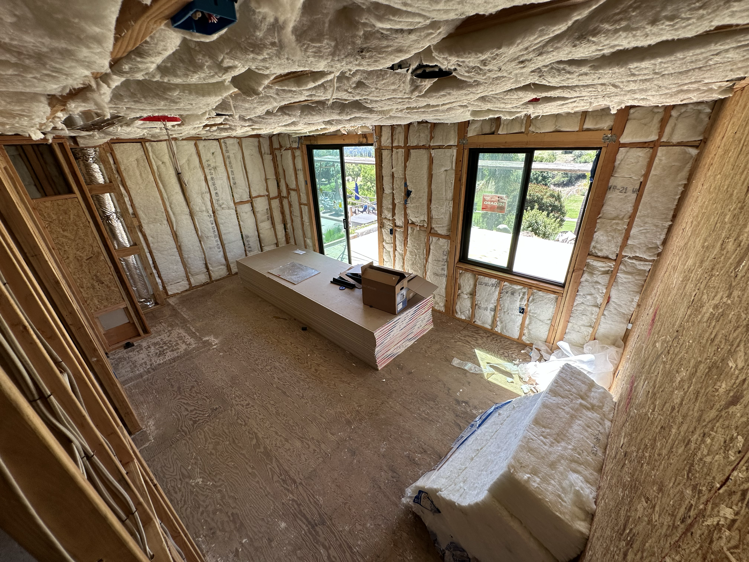 Construction room with insulation material installed in the walls and ceiling, and large windows providing natural light.