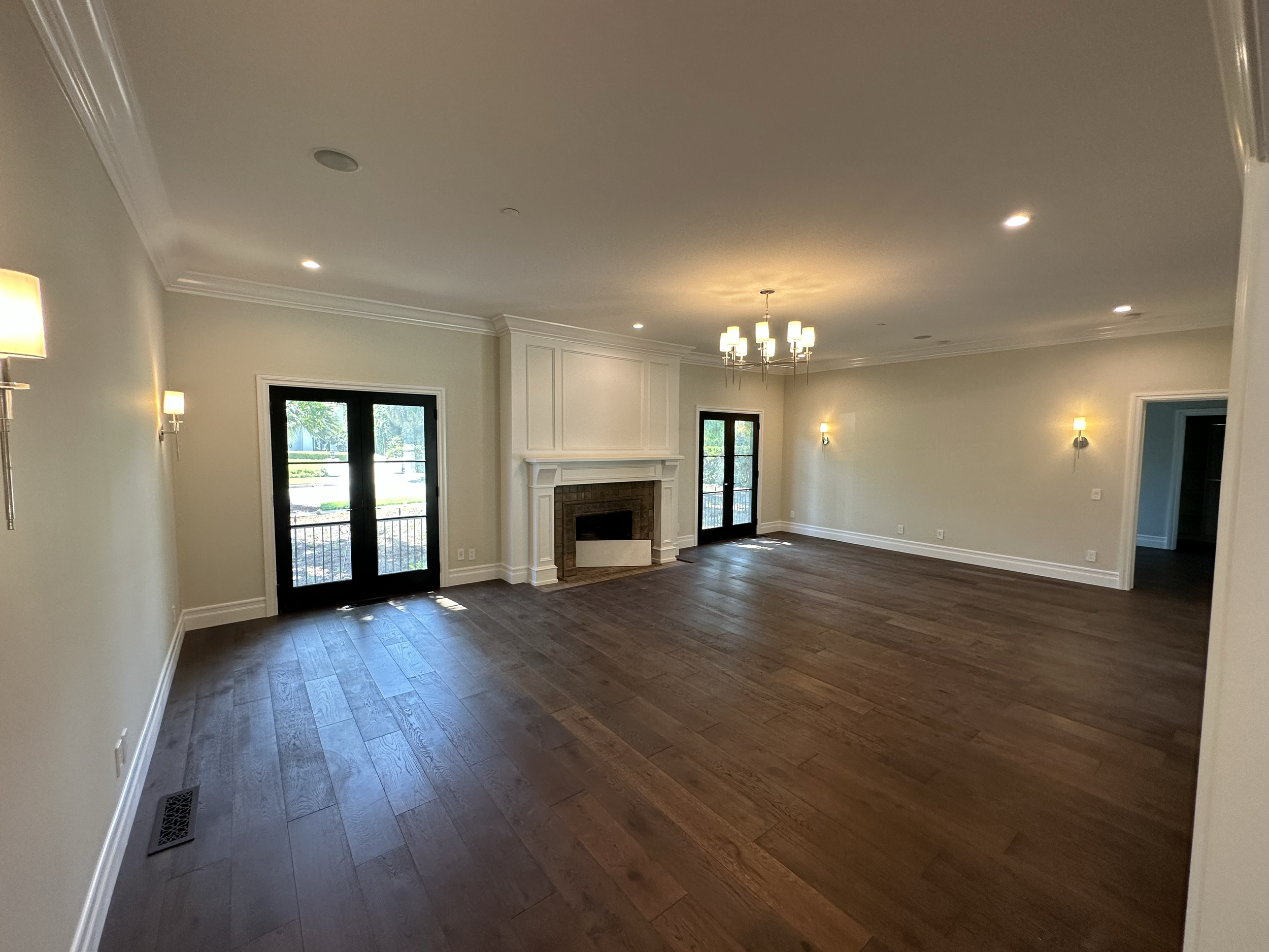 Living room with hardwood floors, white walls, a fireplace, large windows, and ceiling lights.