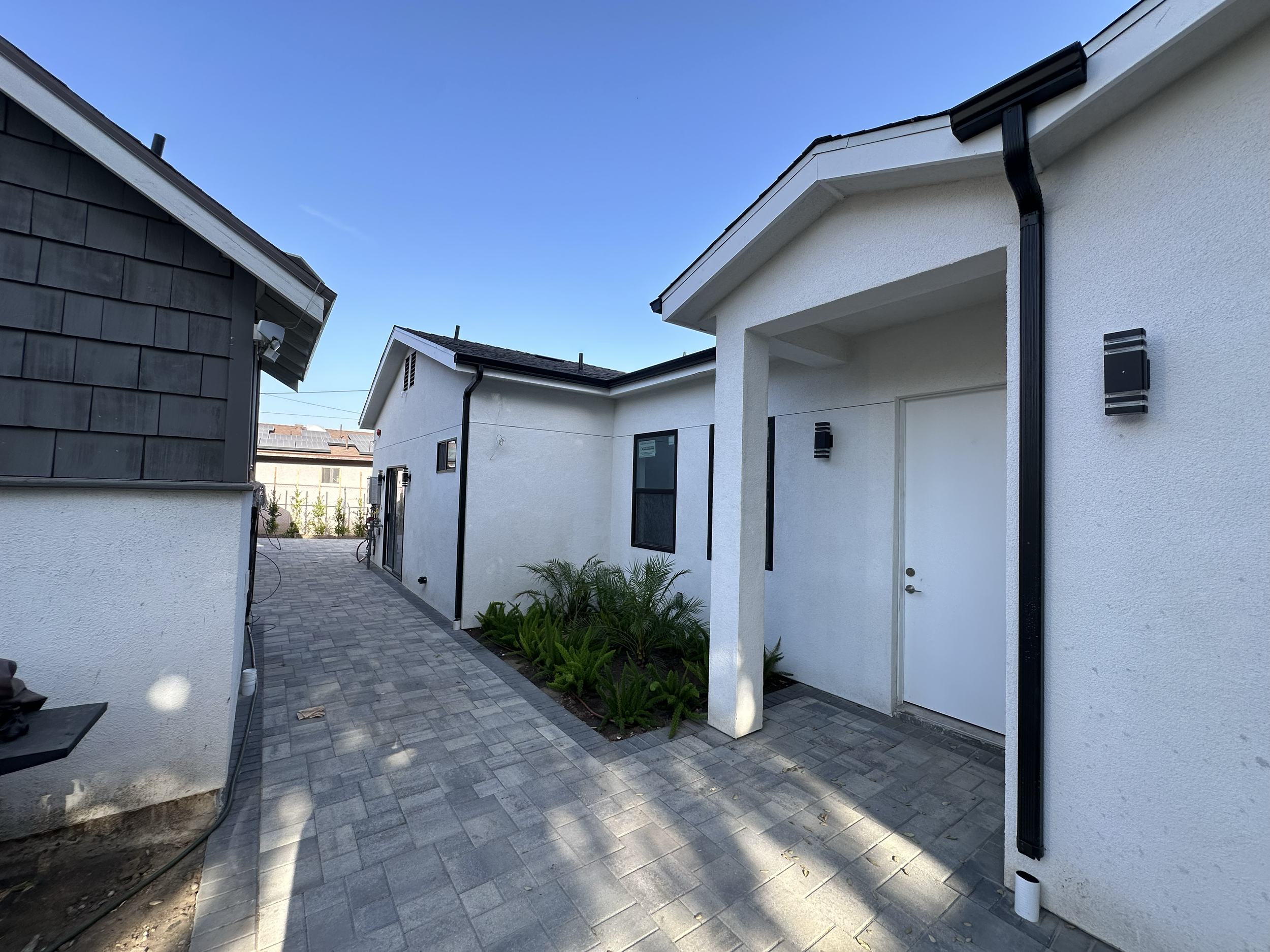 View of modern houses with white stucco walls, black gutters, and a paved courtyard with landscaping and plants.